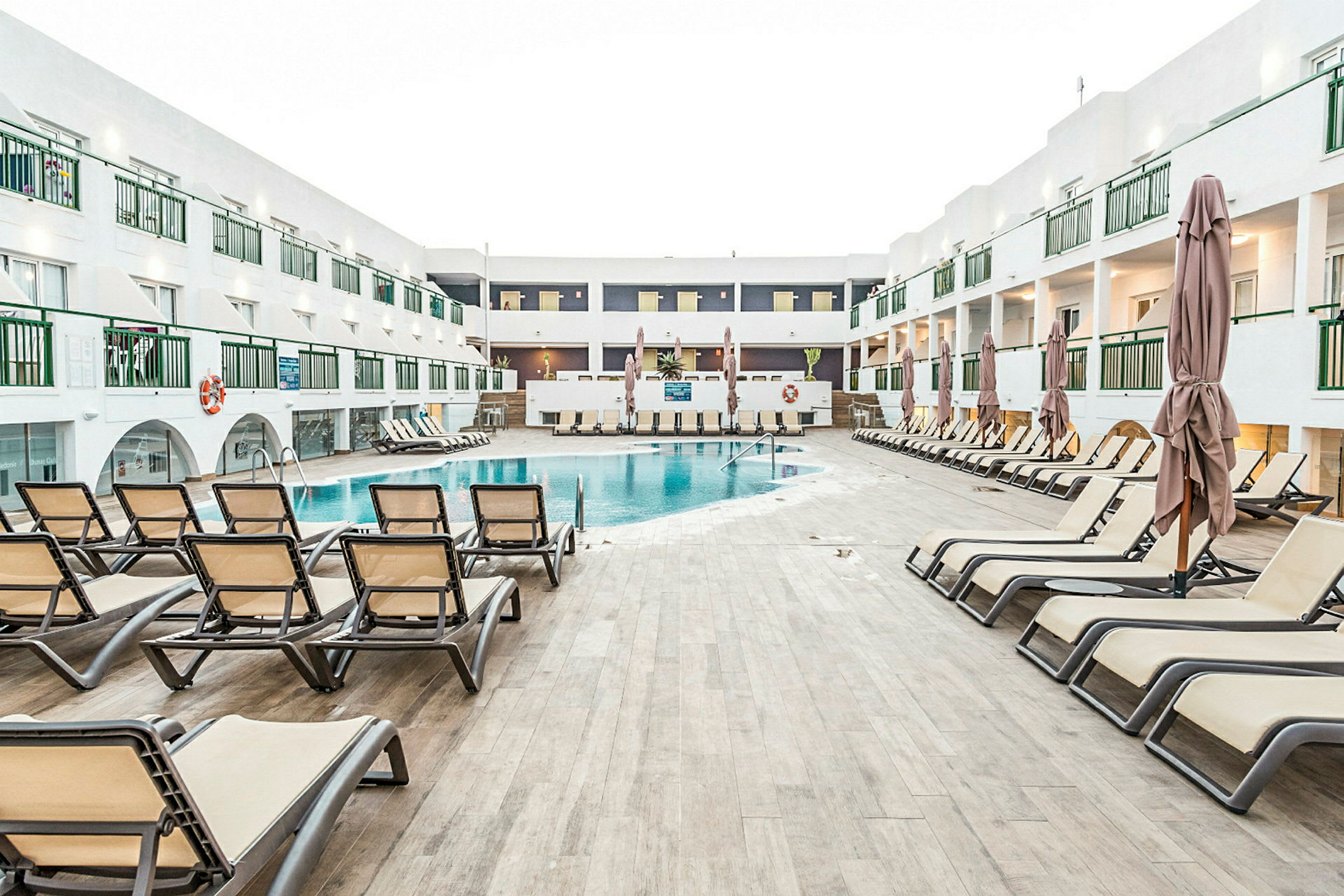Bilde som viser et basseng omgitt av solsenger og et hotellkompleks i bakgrunnen. (AI-generert tekst)