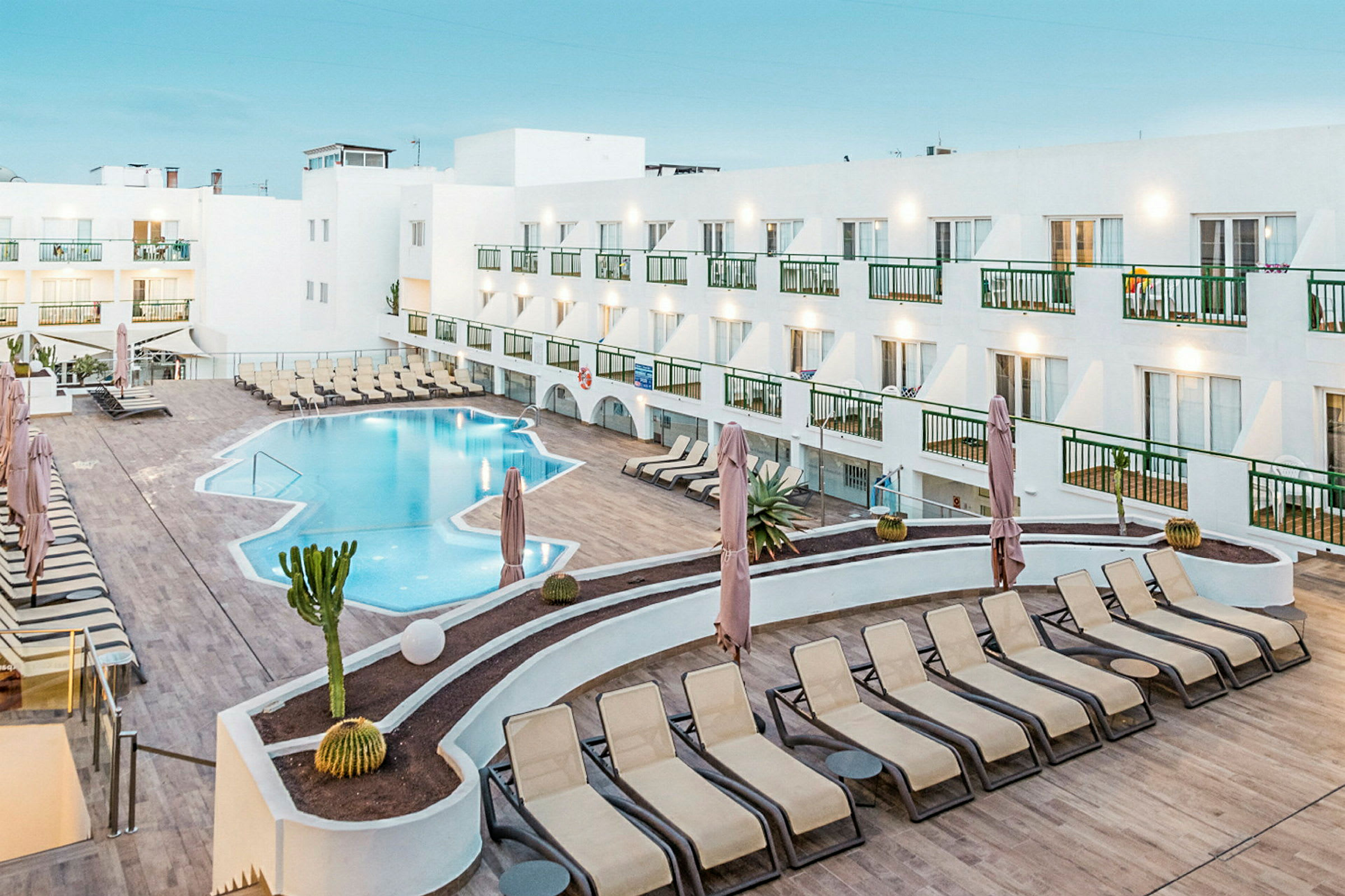 Et hotellbasseng med solsenger og en hvit bygning rundt. (AI-generert tekst)
