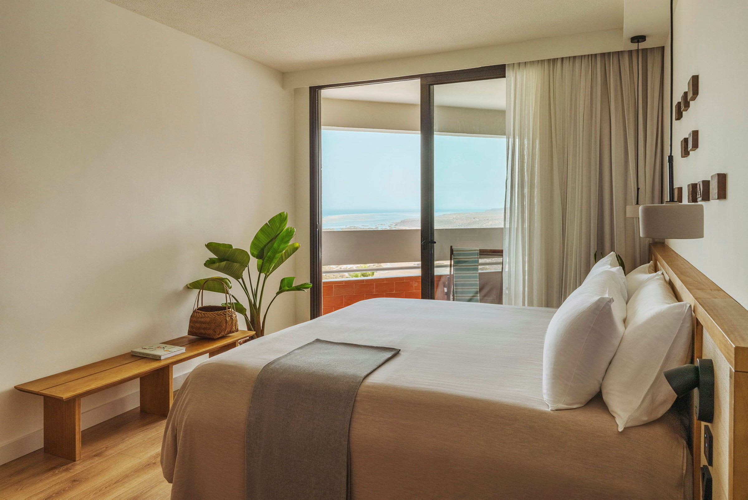 Et lyst og moderne innredet hotellrom med en stor seng og en balkong med utsikt over havet. (AI-generert tekst)