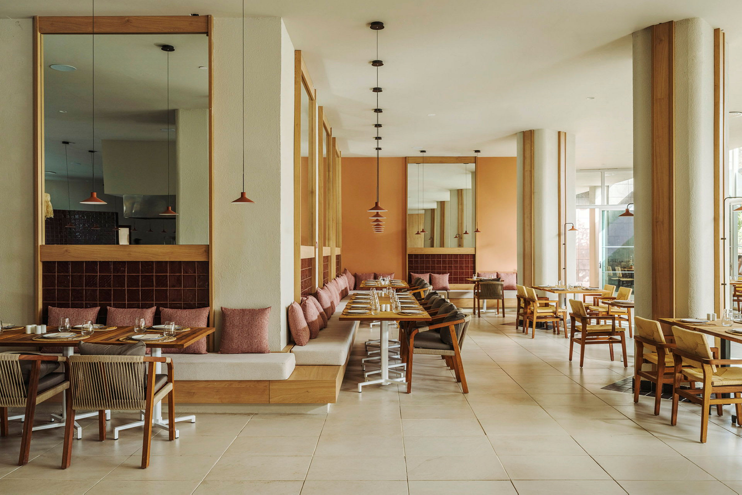 Et moderne innredet restaurantrom med trebord, komfortable stoler og benker dekorert med puter. Veggene er malt i lyse farger, og det er vinduer som slipper inn naturlig lys. (AI-generert tekst)