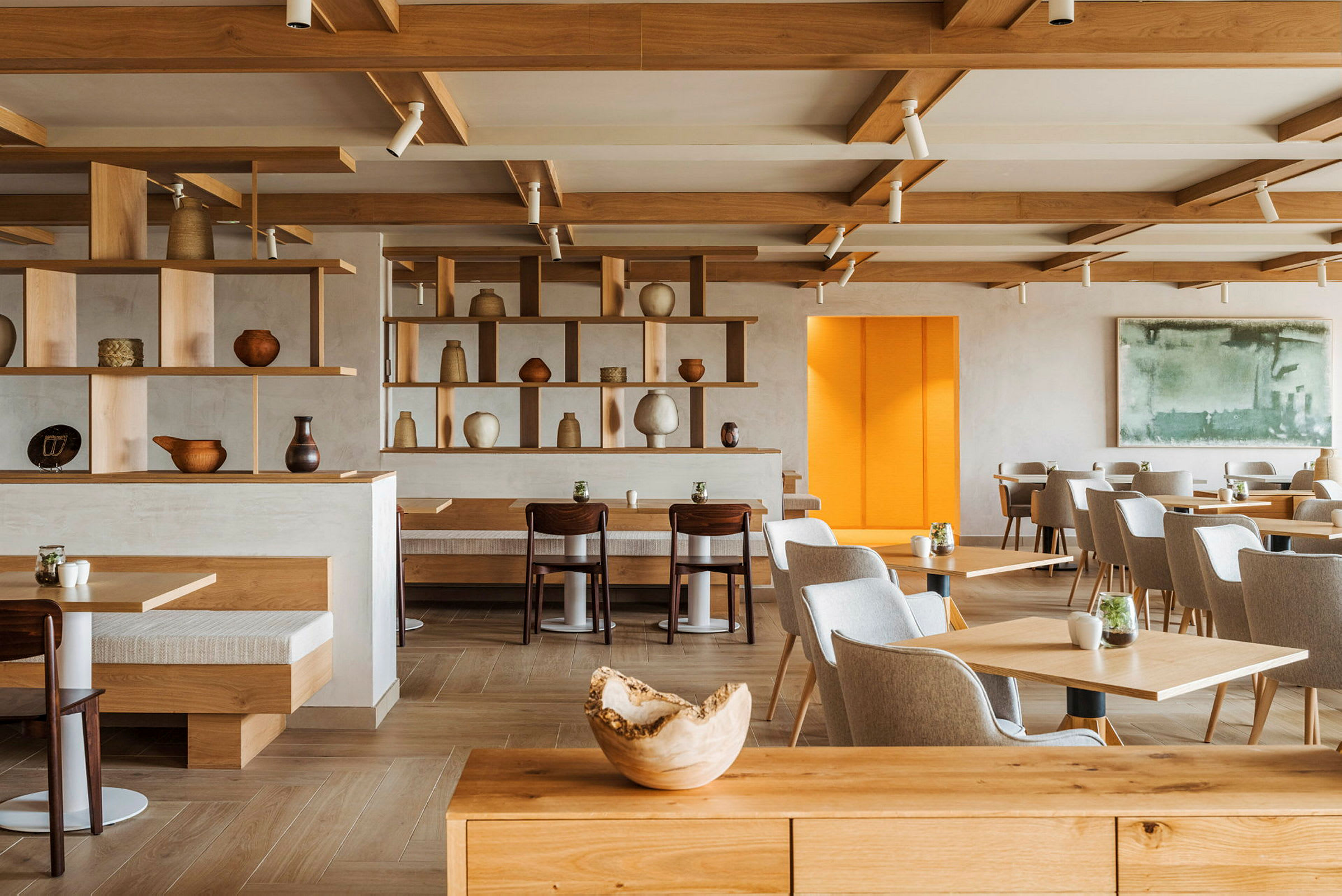 En moderne kafé eller restaurant med møbler i tre, hyller med keramiske gjenstander og flere bord og sitteplasser. (AI-generert tekst)