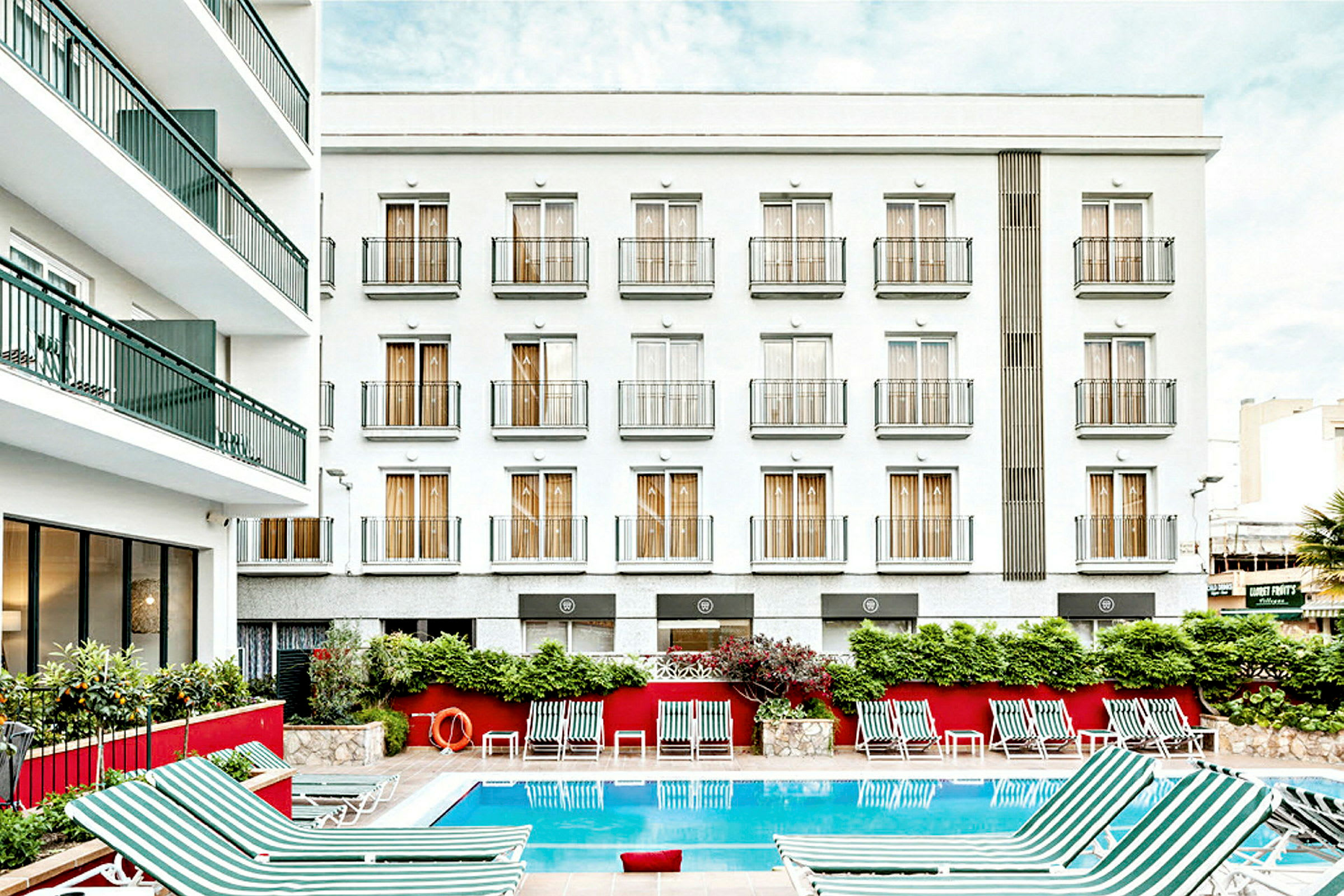 Bilde av en hotellbygning med hvit fasade og flere balkonger. Foran bygningen er et utendørsbasseng med stripete solsenger plassert rundt. (AI-generert tekst)