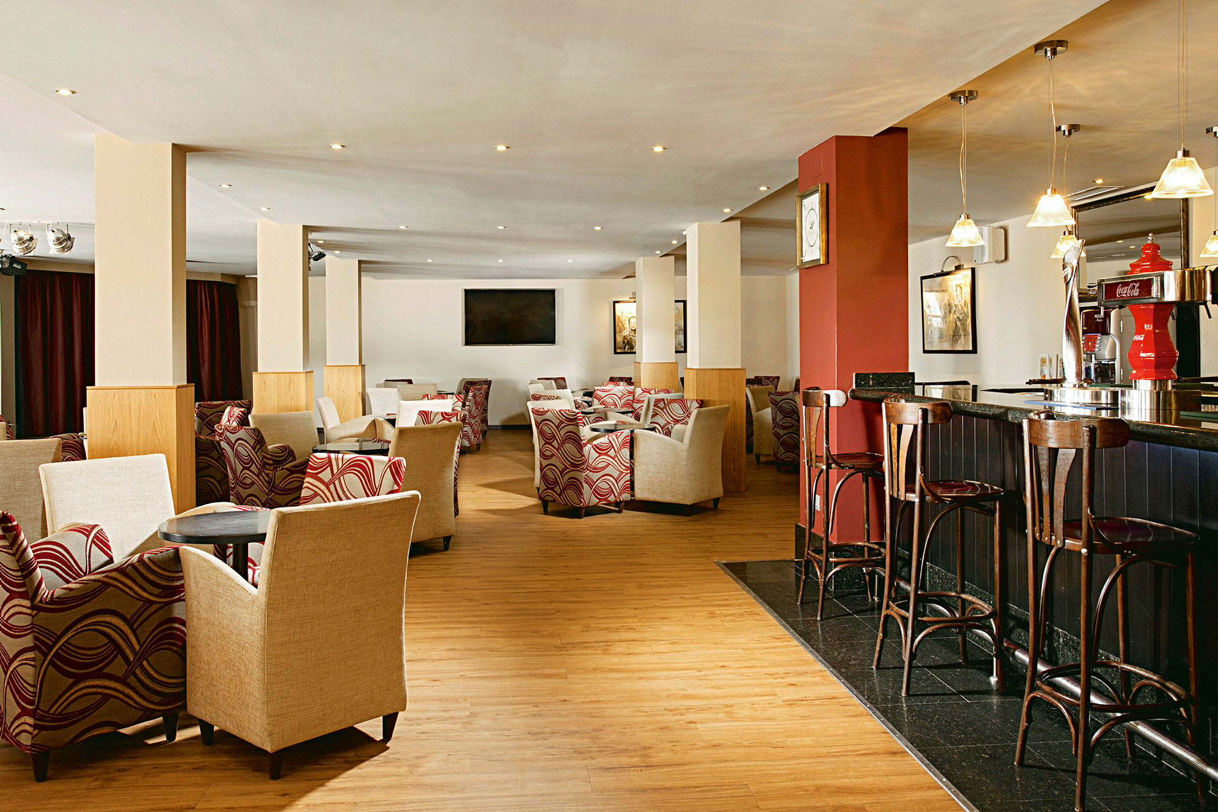 En hotellounge med lenestoler og bord, barkrakker ved en bardisk, og dekorativ innredning. (AI-generert tekst)