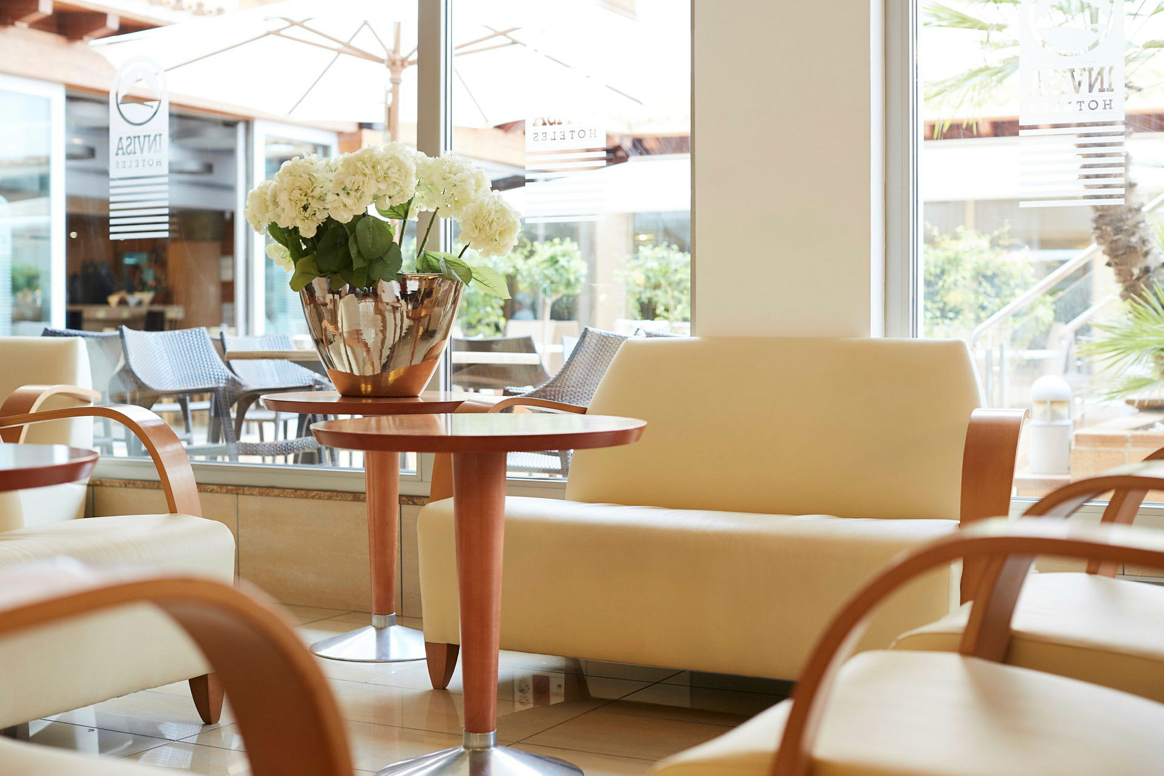Et hotellrom med komfortable sofaer, et trebord og en blomsterpotte med hvite blomster. (AI-generert tekst)