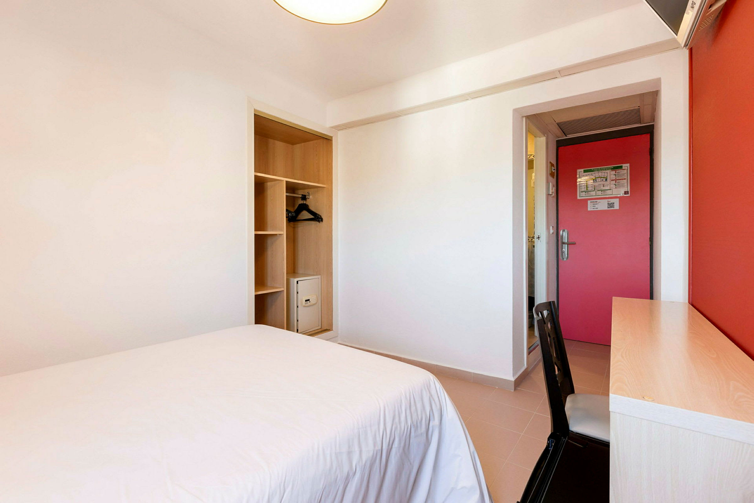 Et hotellrom med en seng, skrivebord og garderobe. (AI-generert tekst)