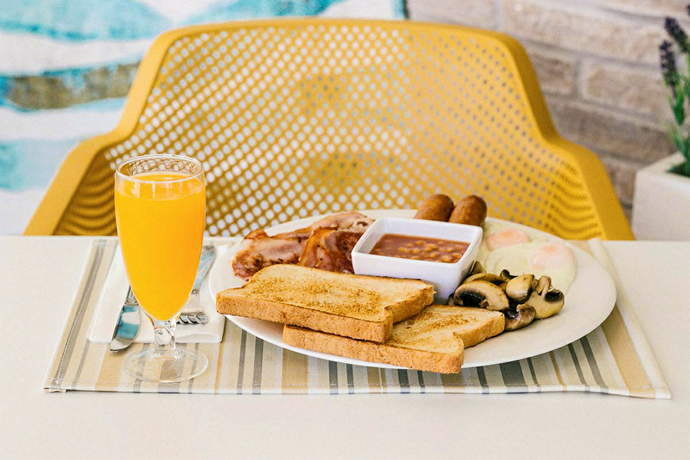 Frokost med ristet brød, stekte egg, pølser, bønner, sopp og appelsinjuice servert ved et bord. (AI-generert tekst)