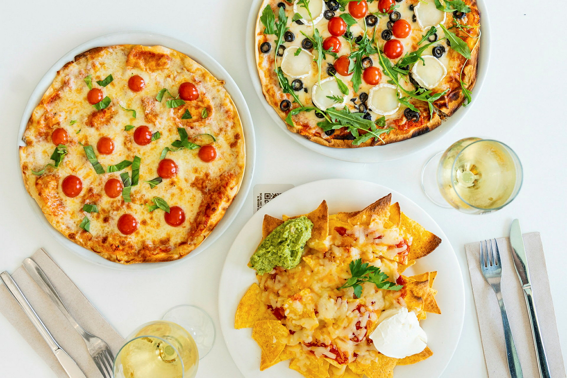 To pizzaer med forskjellige toppinger og en tallerken nachos med guacamole og rømme. (AI-generert tekst)
