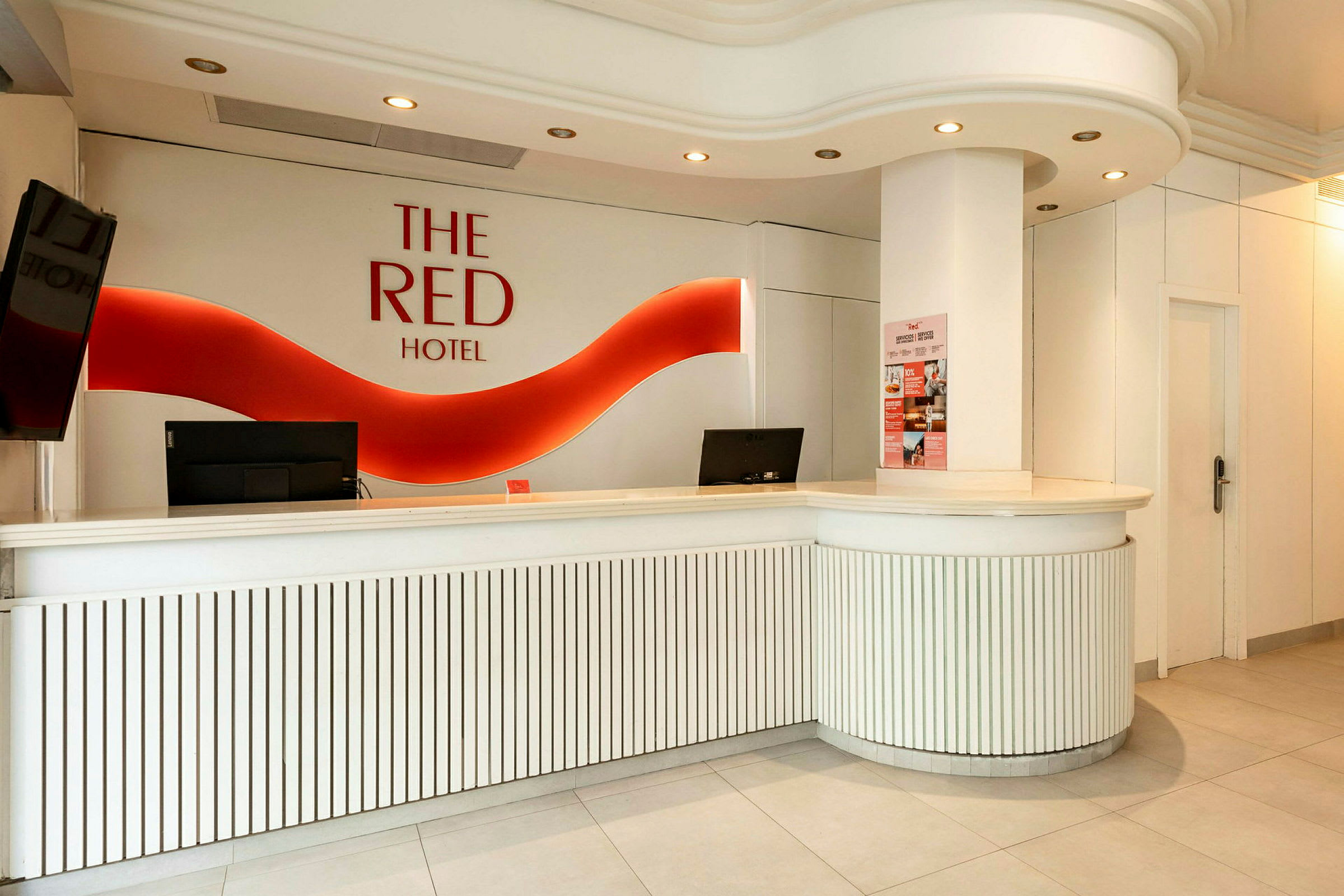 Hotellresepsjon med hvit innredning og rød logo på veggen. (AI-generert tekst)