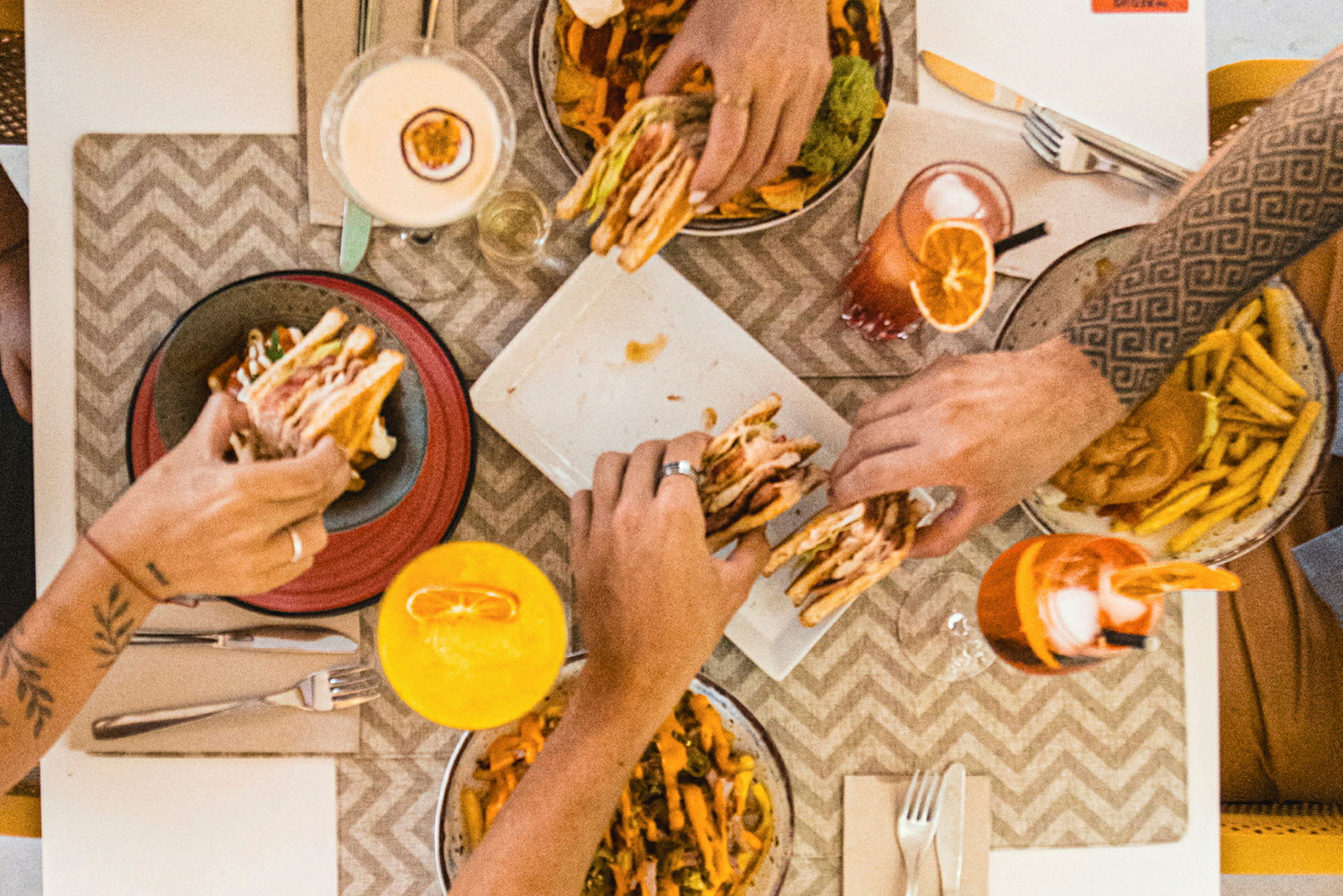 Fire personer spiser hamburgere, pommes frites og drikker fargerike drikker ved et bord. (AI-generert tekst)