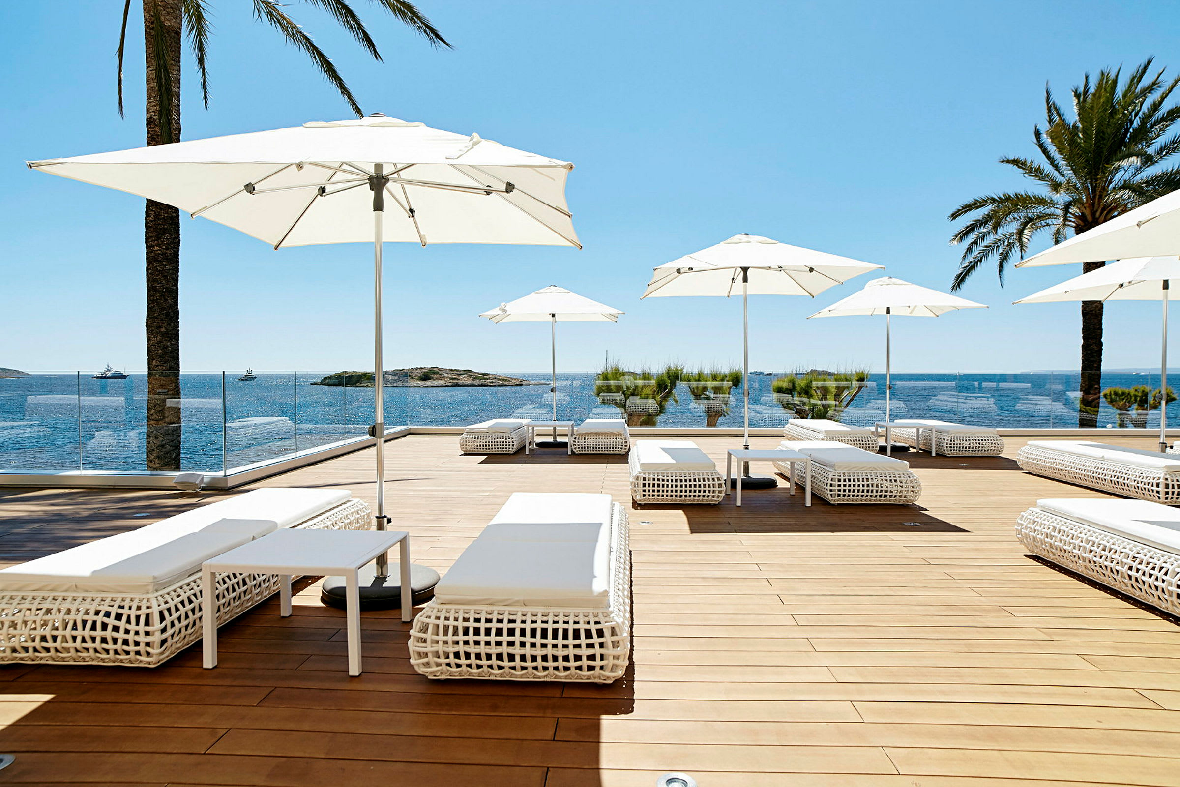Solterrasse med hvite solsenger og parasoller, utsikt over havet og blå himmel. (AI-generert tekst)