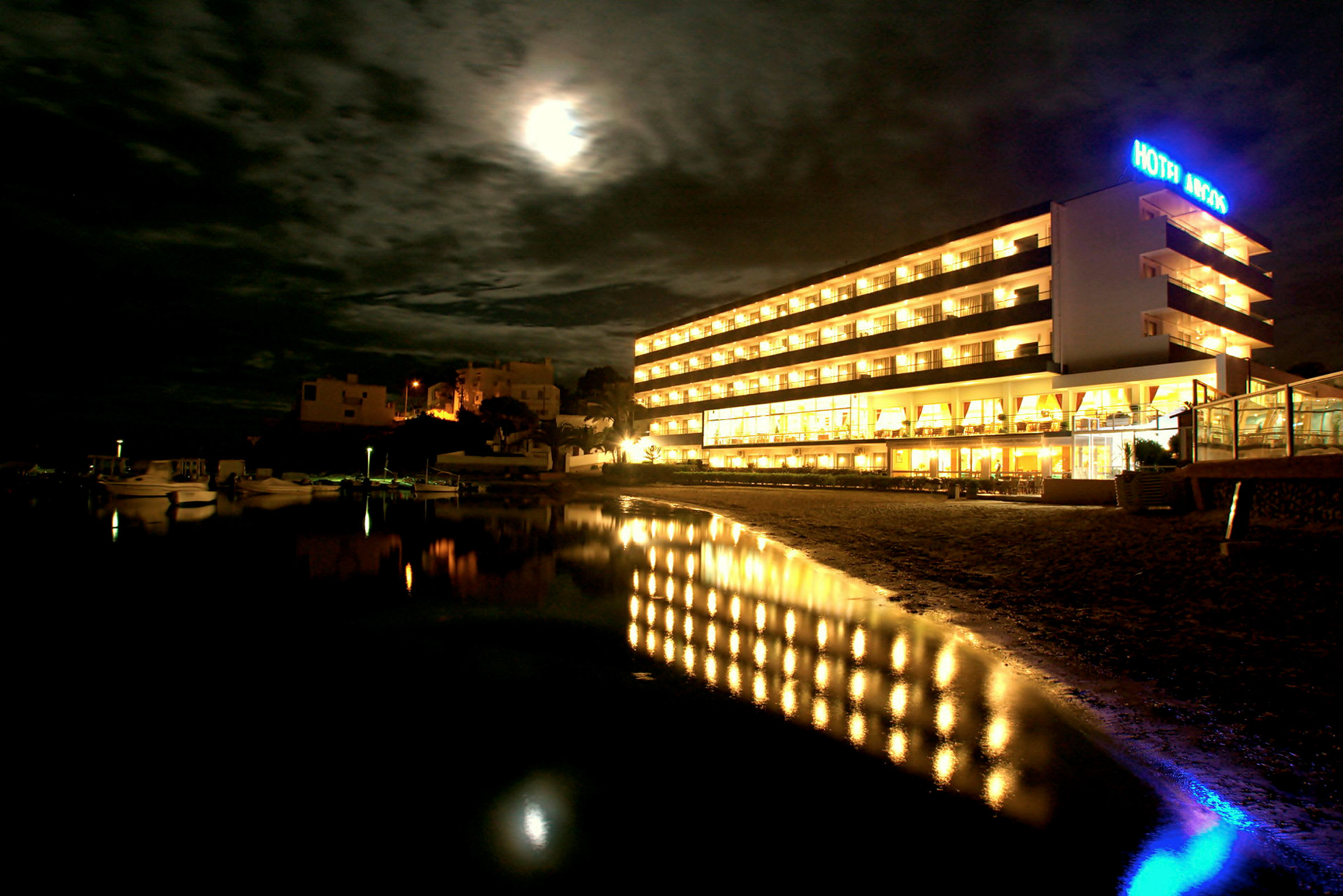 Et hotell opplyst om natten med en refleksjon i vannet foran. (AI-generert tekst)