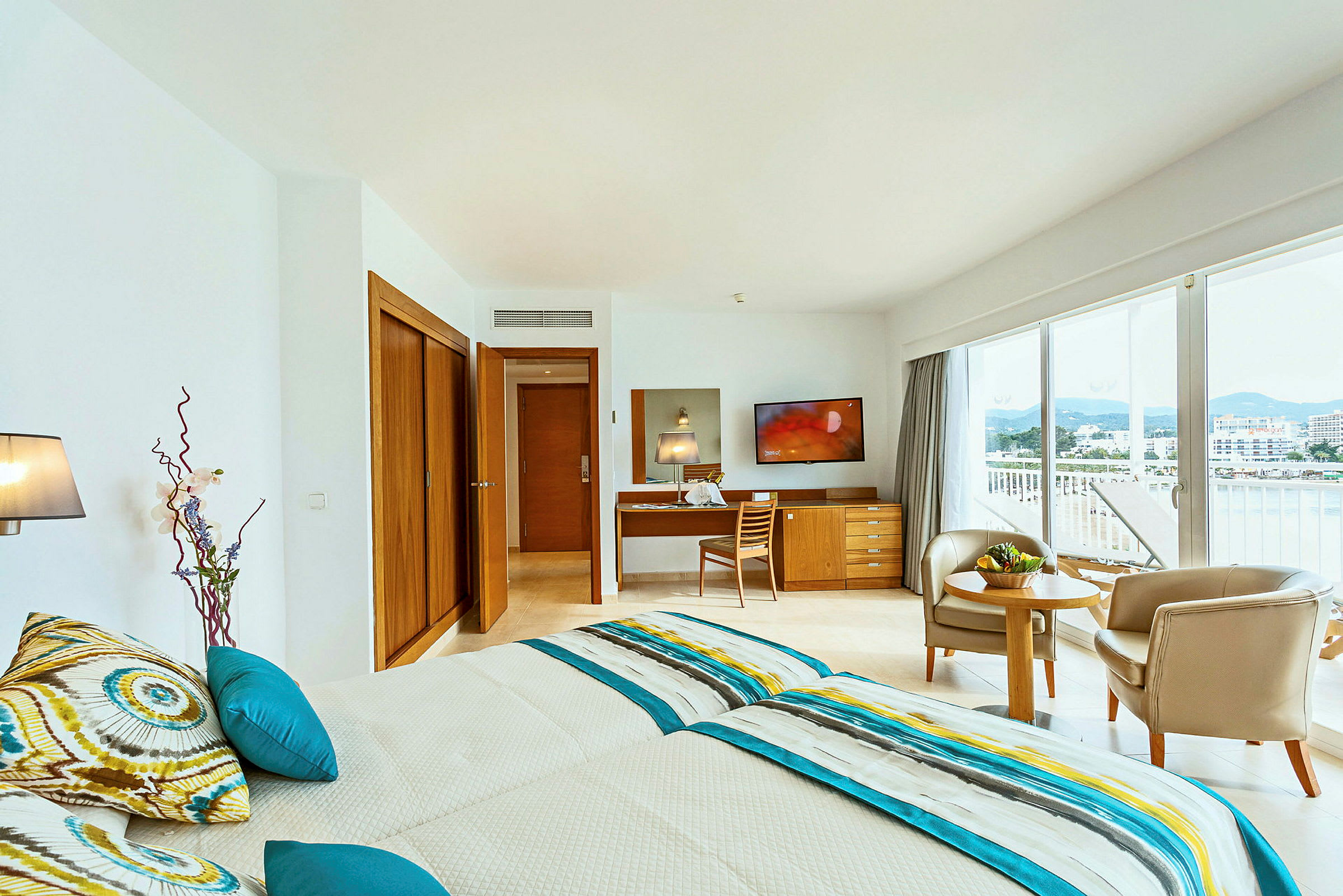 Et lyst og moderne innredet hotellrom med to enkeltsenger, en sittegruppe og store vinduer med utsikt. (AI-generert tekst)