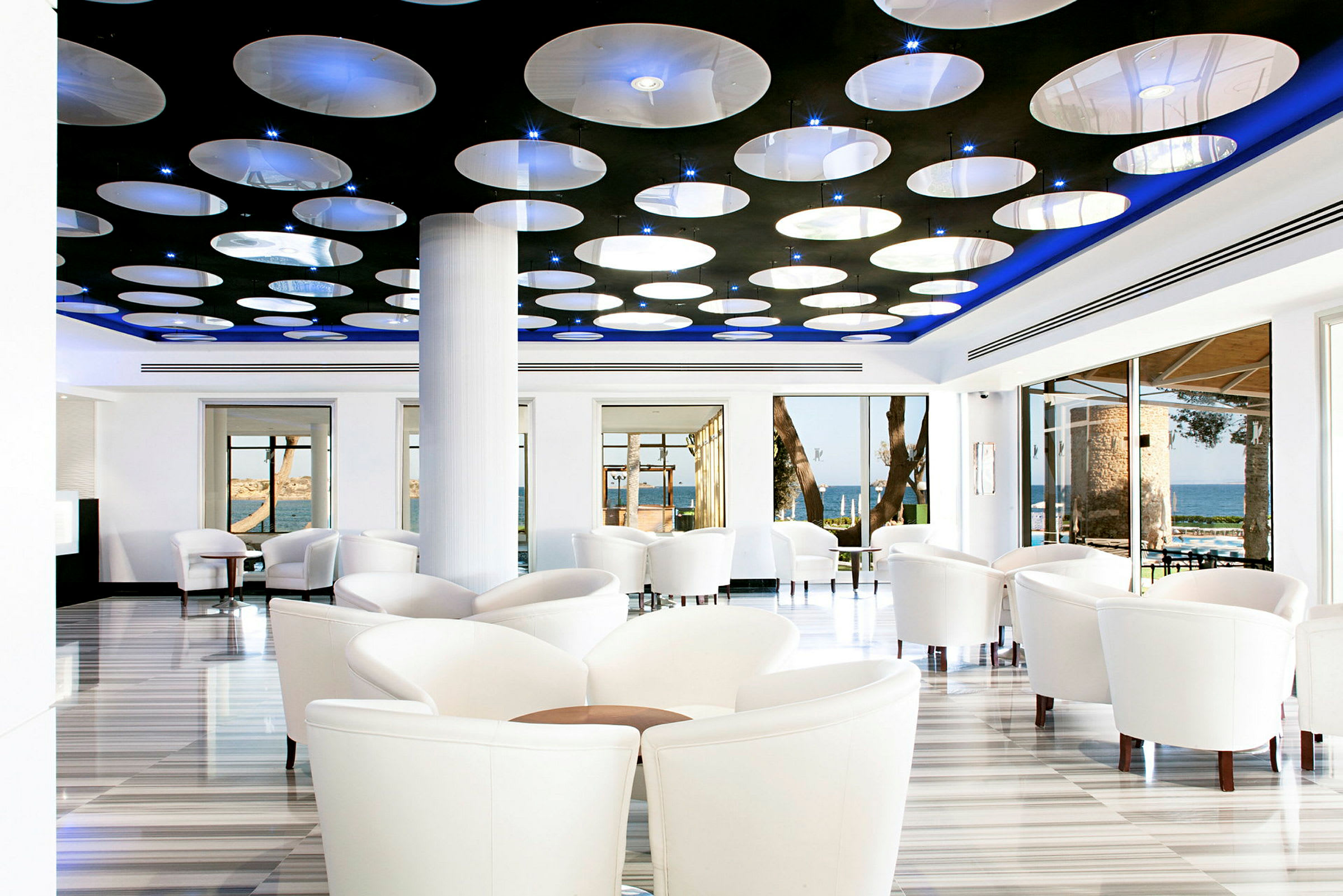En moderne innredet kafé eller lounge med hvite stoler, store vinduer og et takkonstruksjon med runde lamper. (AI-generert tekst)