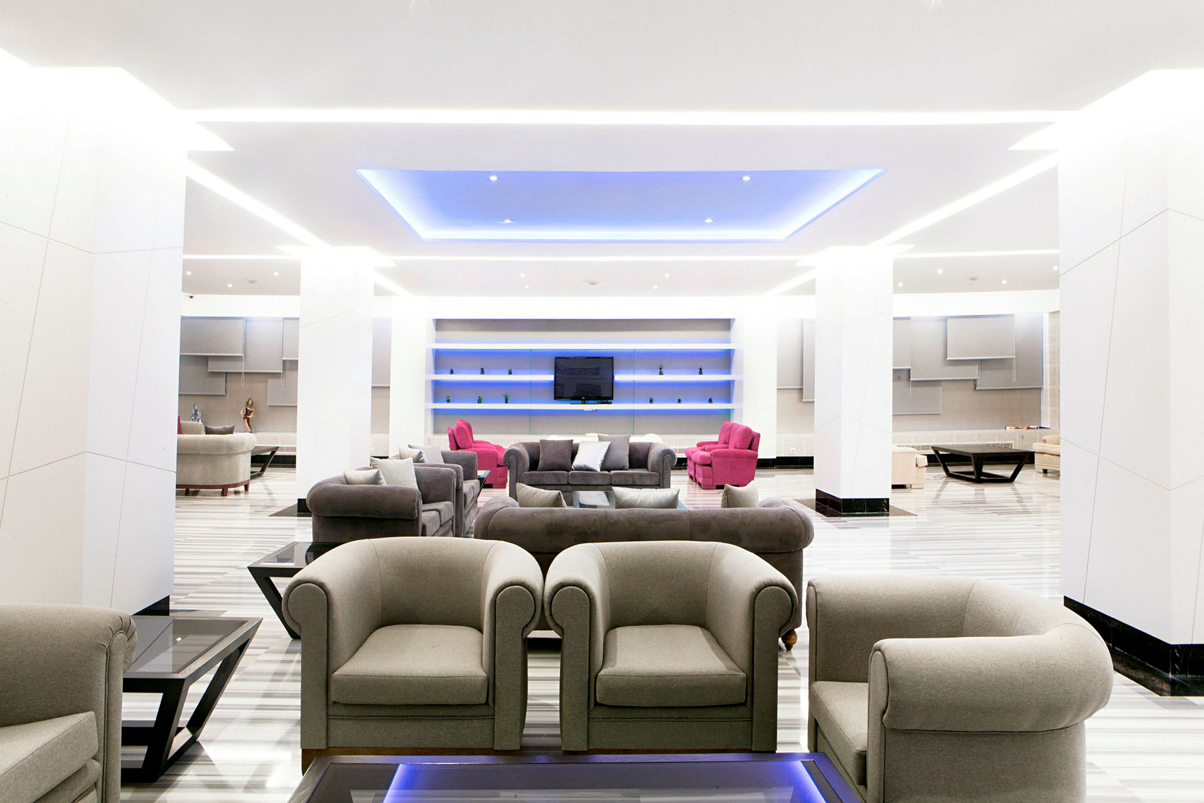 En moderne lounge med grå og rosa sittemøbler samt blå takbelysning. (AI-generert tekst)