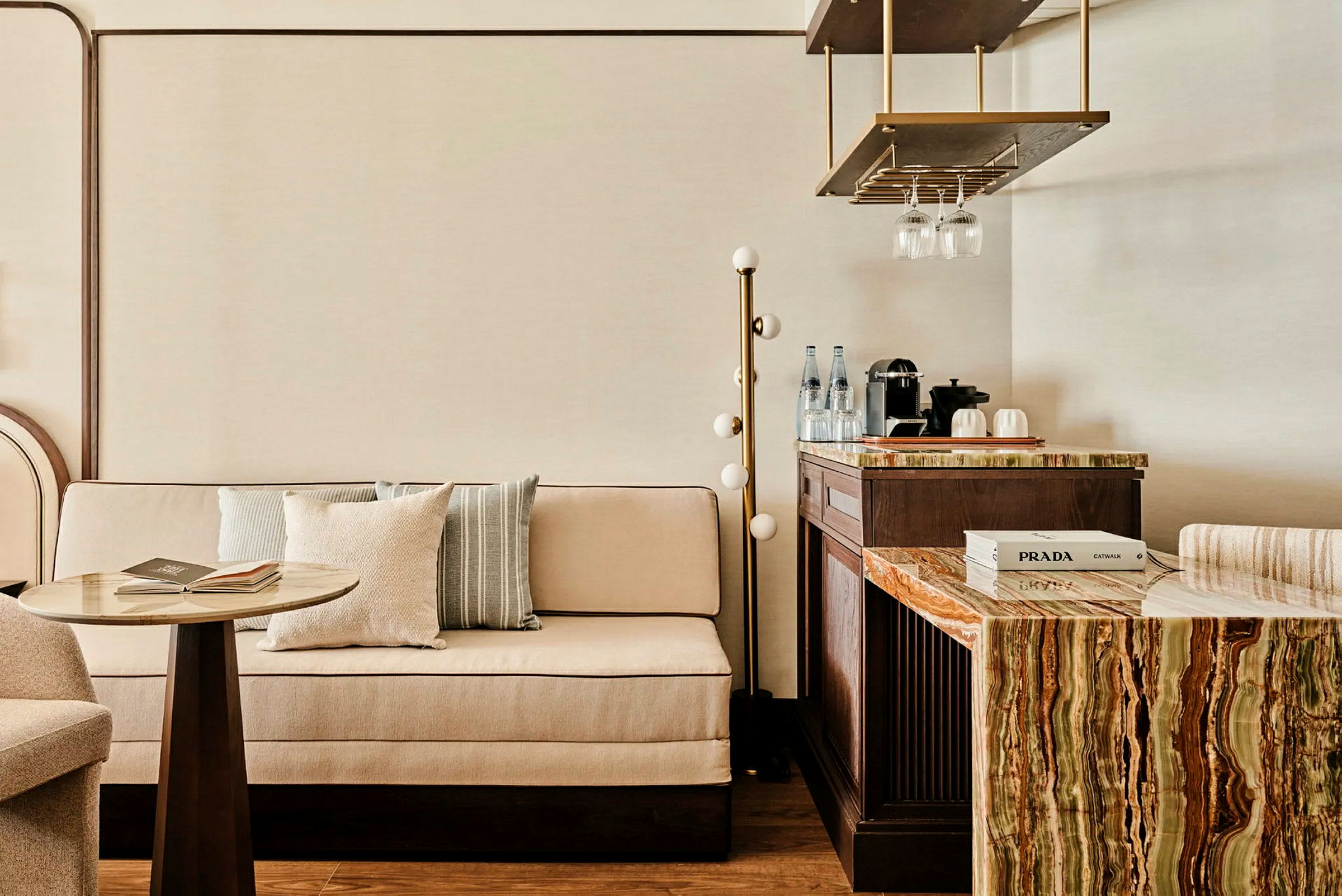 En elegant innredet sittegruppe med en sofa, et lite bord og en benk med en marmorert overflate samt en kaffemaskin og glass. (AI-generert tekst)