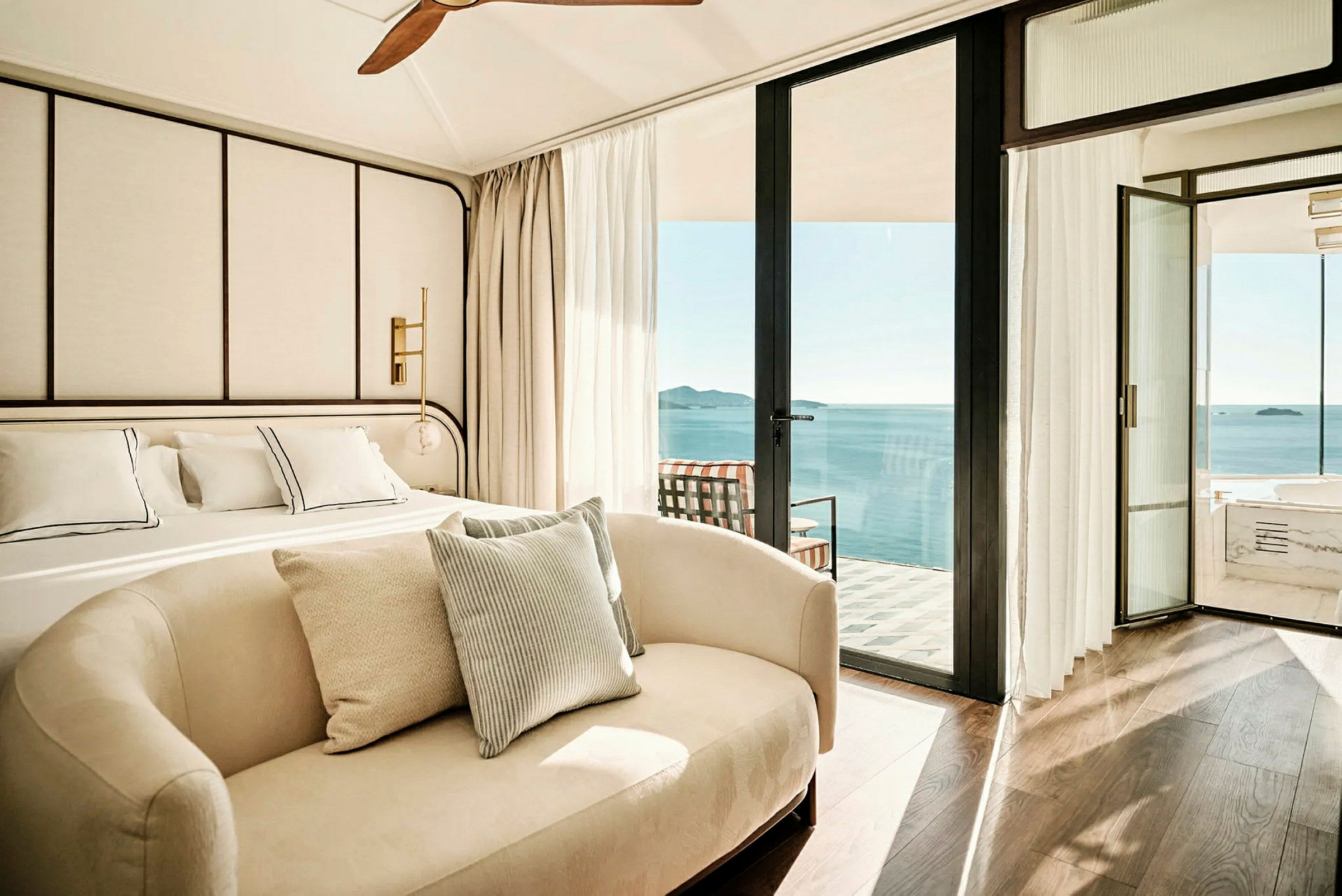 Moderne innredet hotellrom med stor seng, sofa og utsikt over havet fra en balkong. (AI-generert tekst)