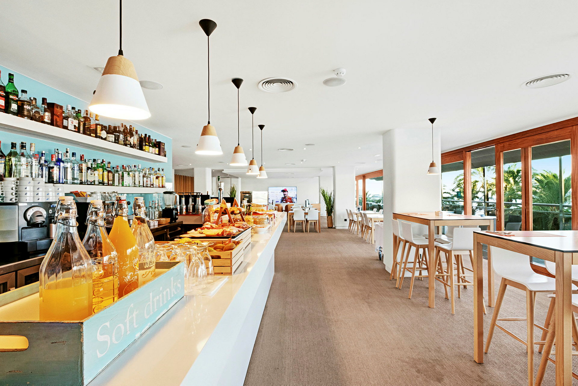 Interiørbilde av en moderne bar og kafé med bord, stoler og store vinduer og en serveringsdisk. (AI-generert tekst)