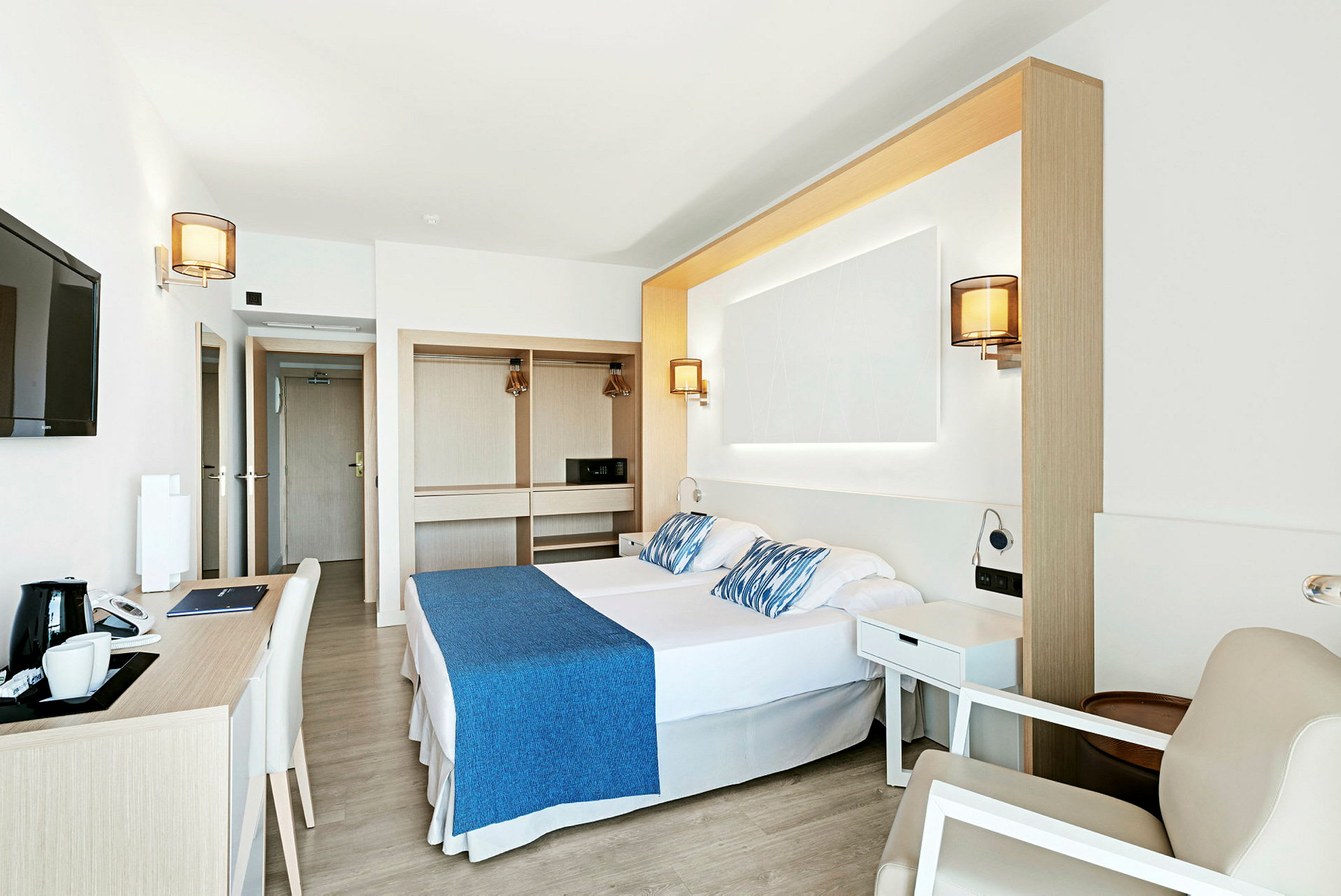Et lyst og moderne hotellrom med dobbeltseng, skrivebord og garderobe. (AI-generert tekst)