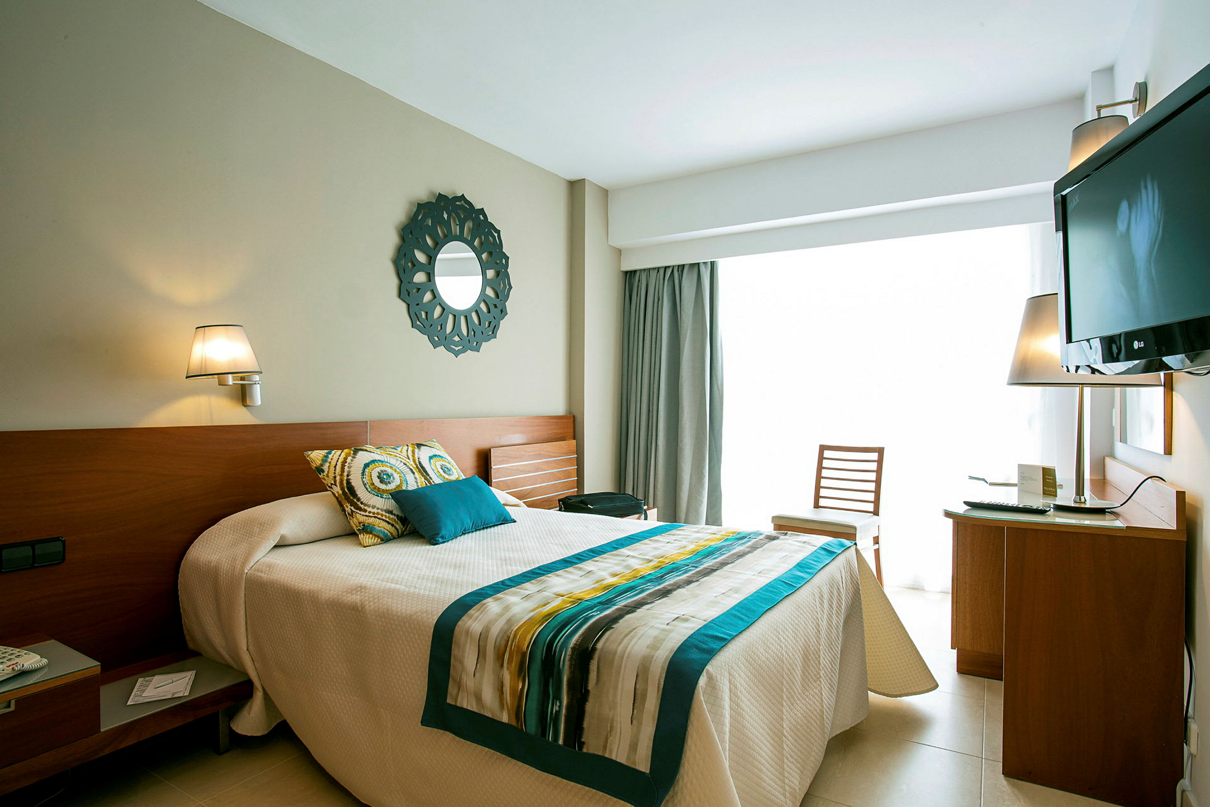 Et lyst og moderne hotellrom med seng, dekorative puter, en TV og et skrivebord. (AI-generert tekst)