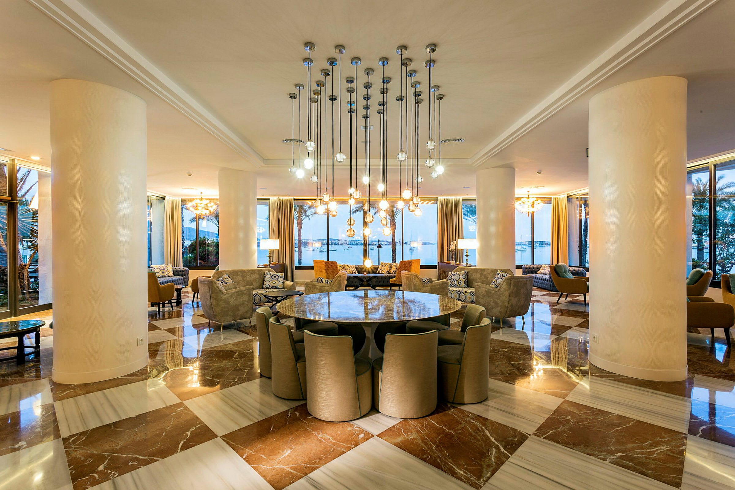 En elegant innredet hotellobby med marmor gulv, moderne lysarmaturer og et glassbord med stoler. (AI-generert tekst)