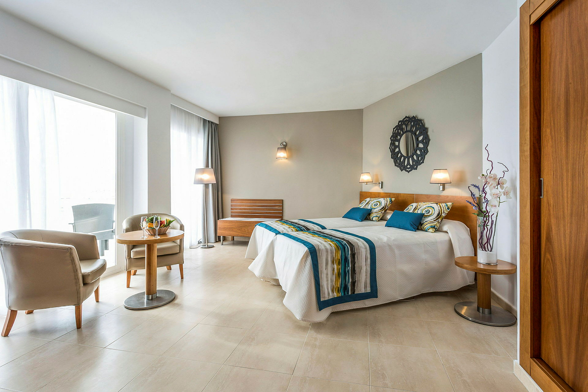 Et romslig og lyst hotellrom med en dobbeltseng, sittegruppe, store vinduer og moderne innredning. (AI-generert tekst)