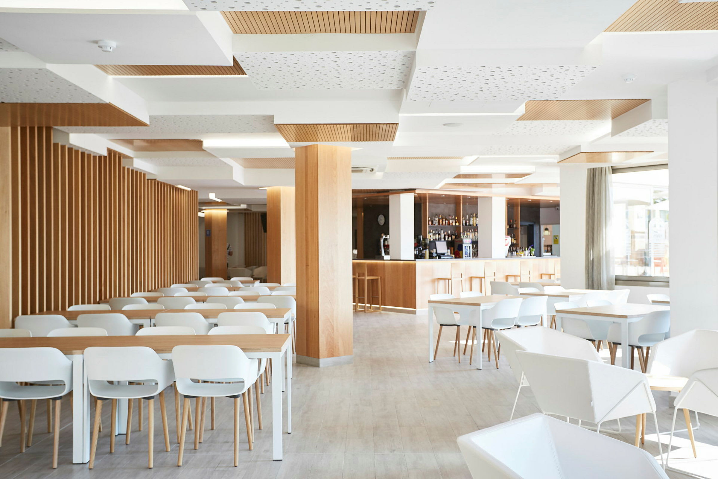 En lys og moderne restaurant med hvite stoler og bord, tredetaljer og en bardisk. (AI-generert tekst)