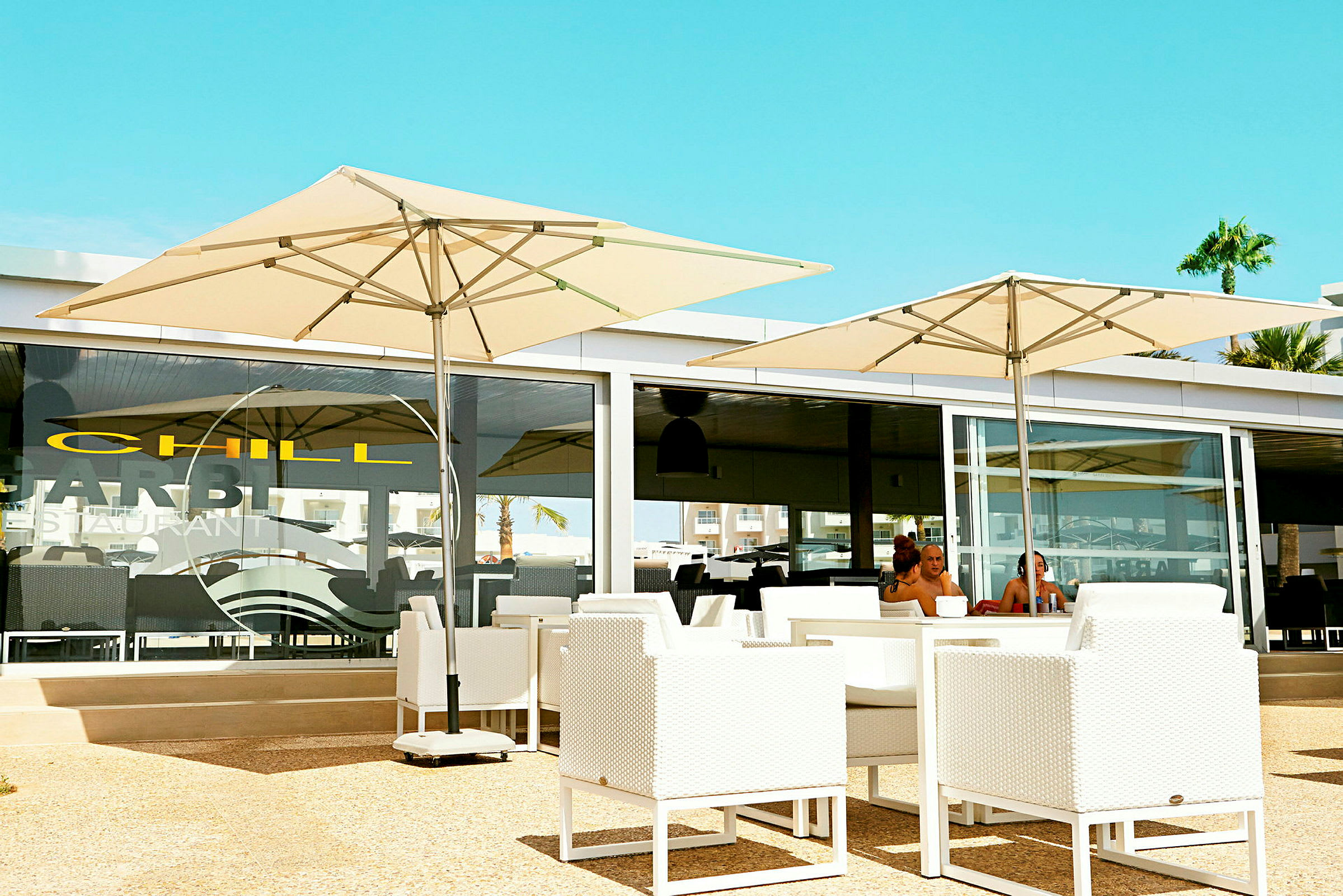 En restaurantterrasse med hvite møbler og store parasoller. (AI-generert tekst)