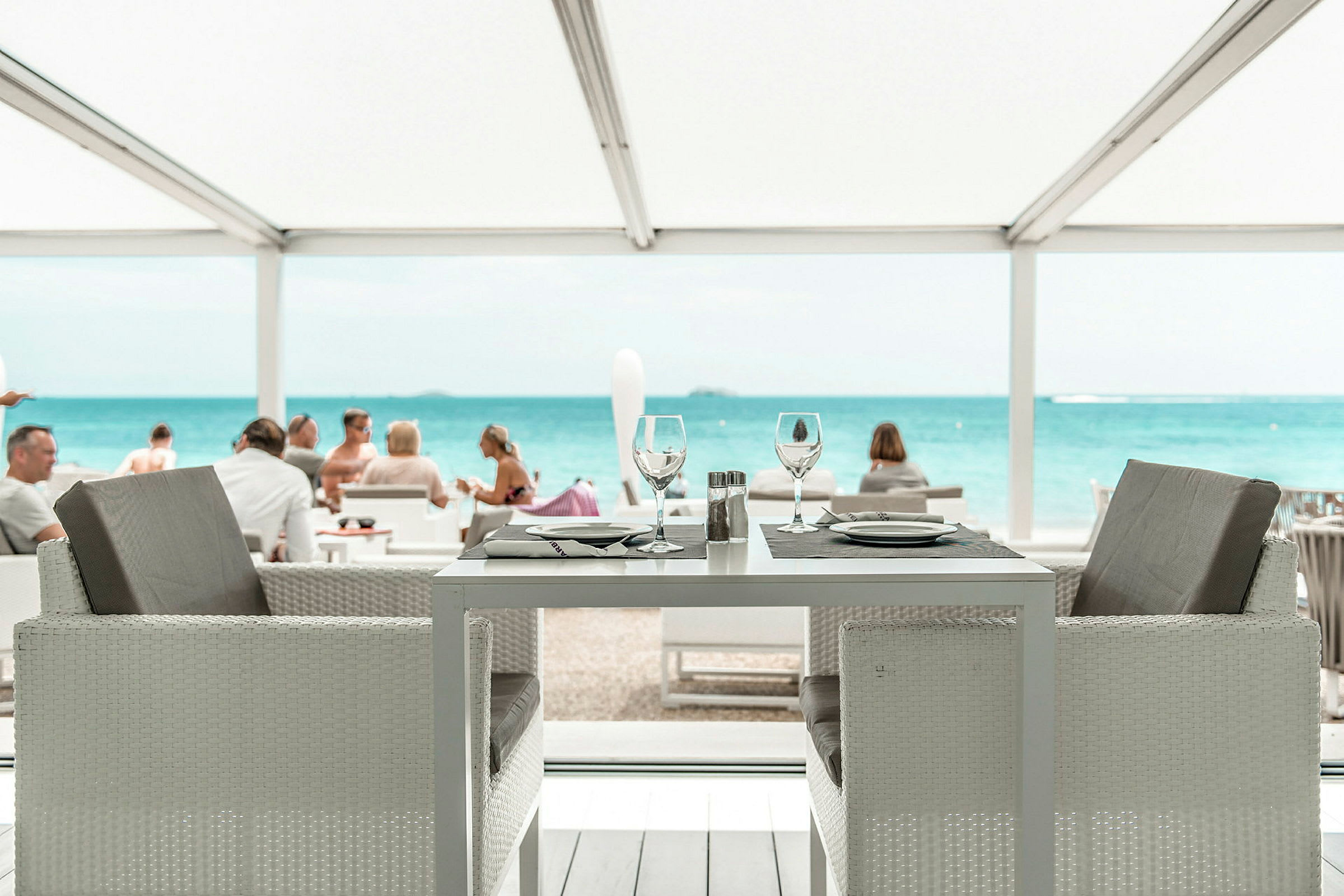 Et dekket restaurantbord med utsikt over havet og en strand. (AI-generert tekst)