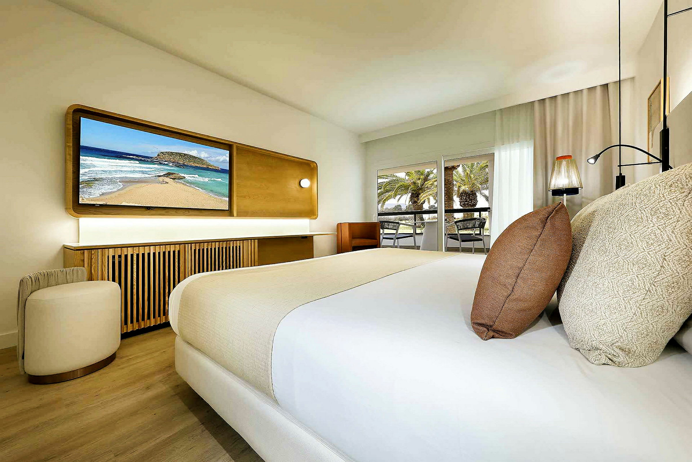 Et moderne hotellrom med en dobbeltseng, en TV på veggen og en balkong med utsikt over palmer. (AI-generert tekst)