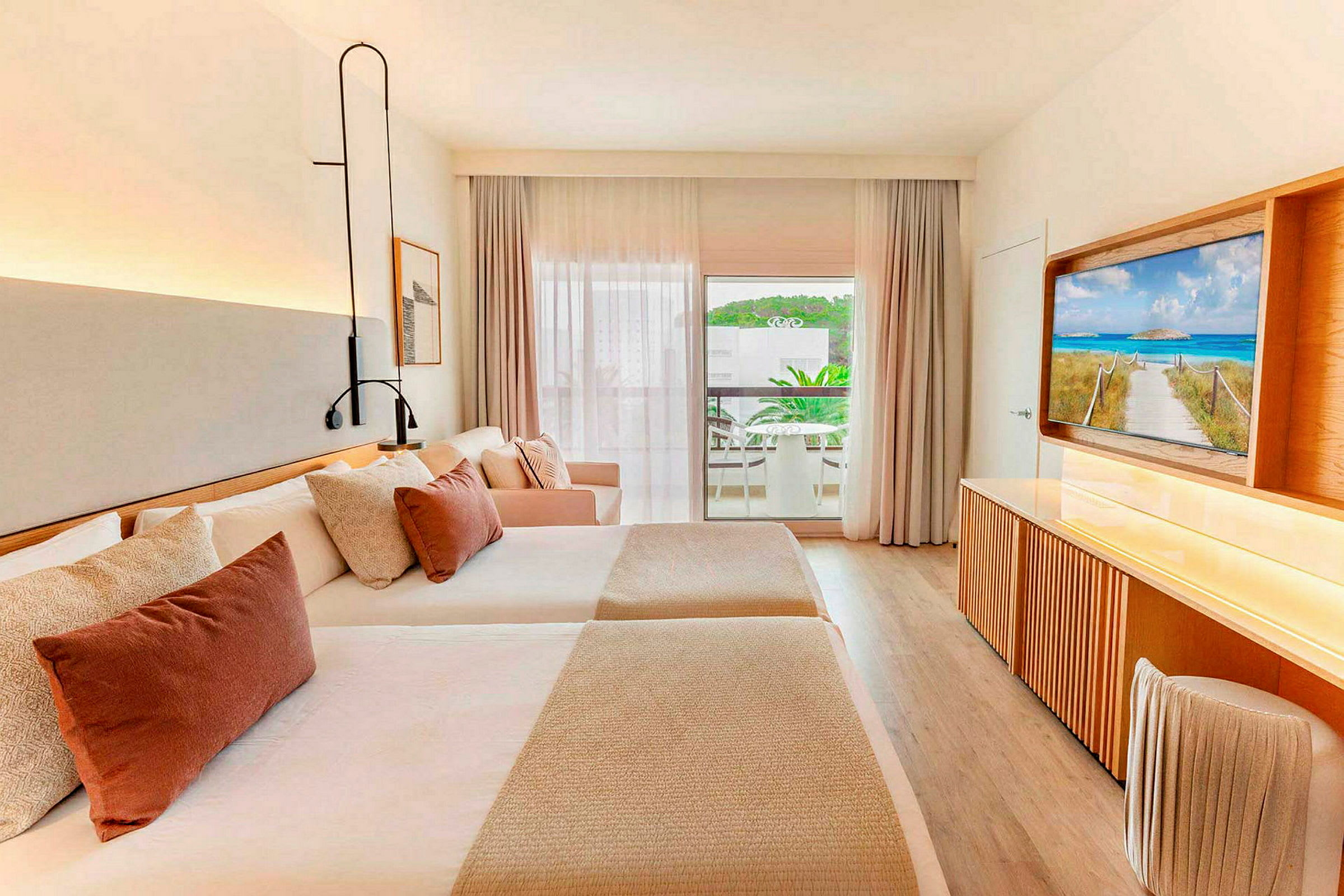 Et hotellrom med to senger, en sofa og en TV, samt en balkong med uteplass utenfor. (AI-generert tekst)