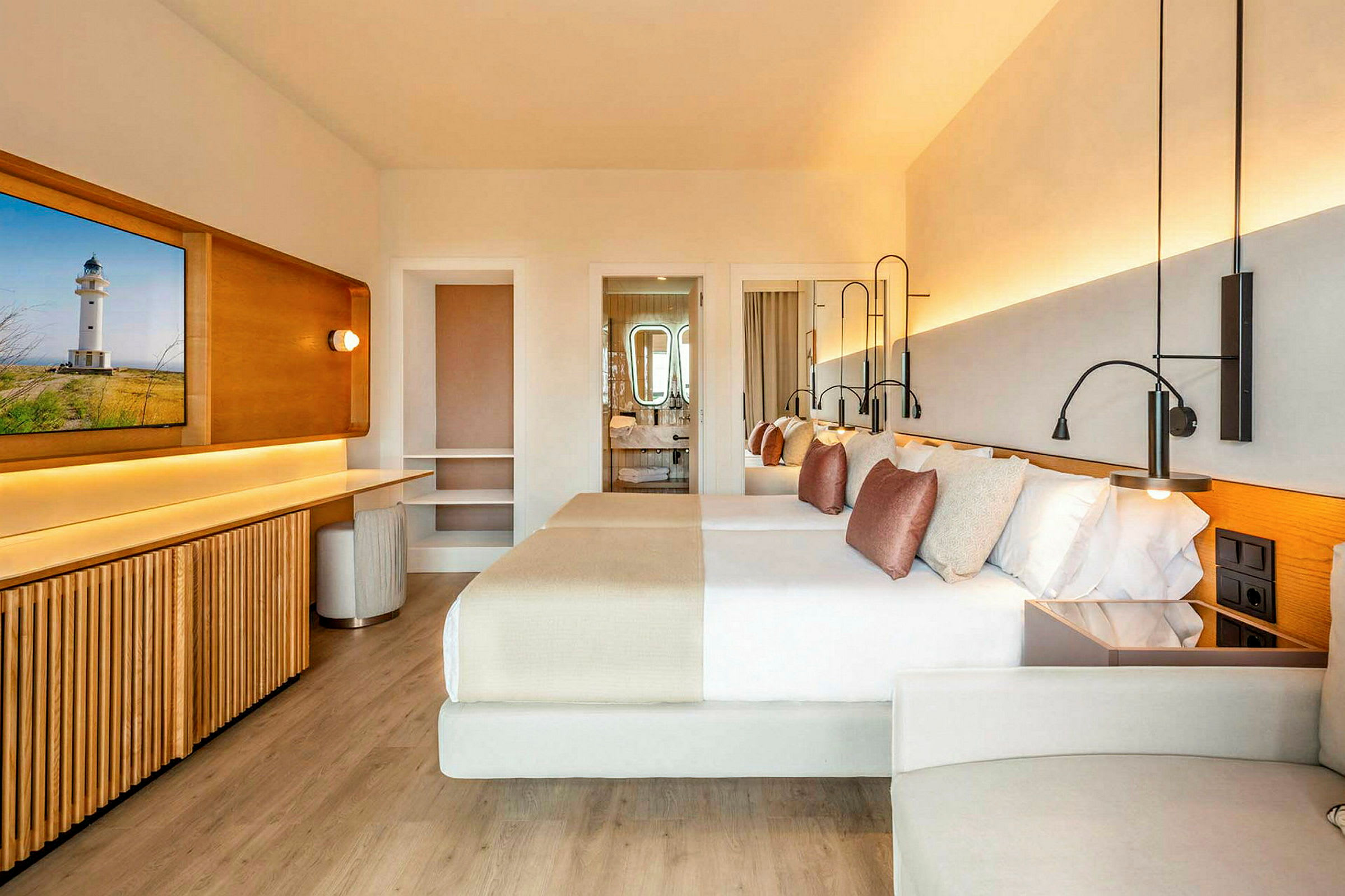 Et moderne hotellrom med lys innredning, to dobbeltsenger med dekorative puter, et skrivebord og et bad i bakgrunnen. (AI-generert tekst)