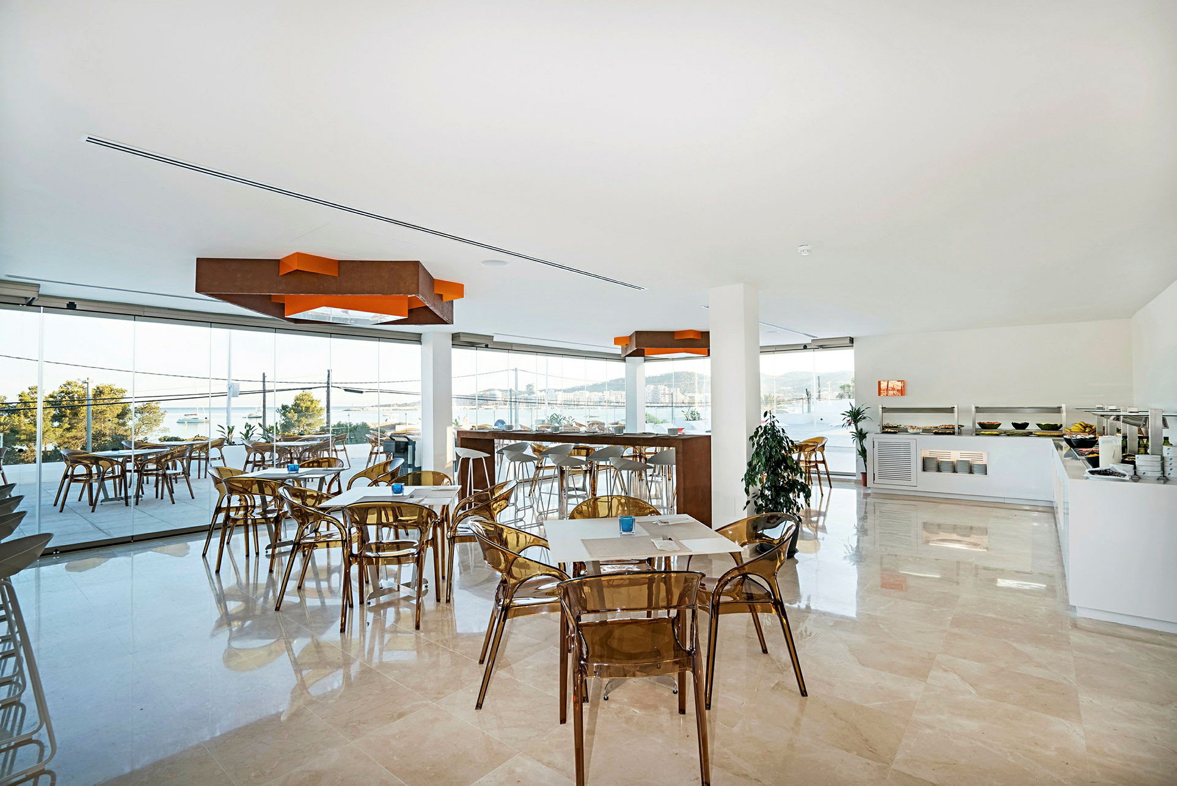 Interiør av en lys restaurant med glassvegger og utsikt over vann og landskap. (AI-generert tekst)