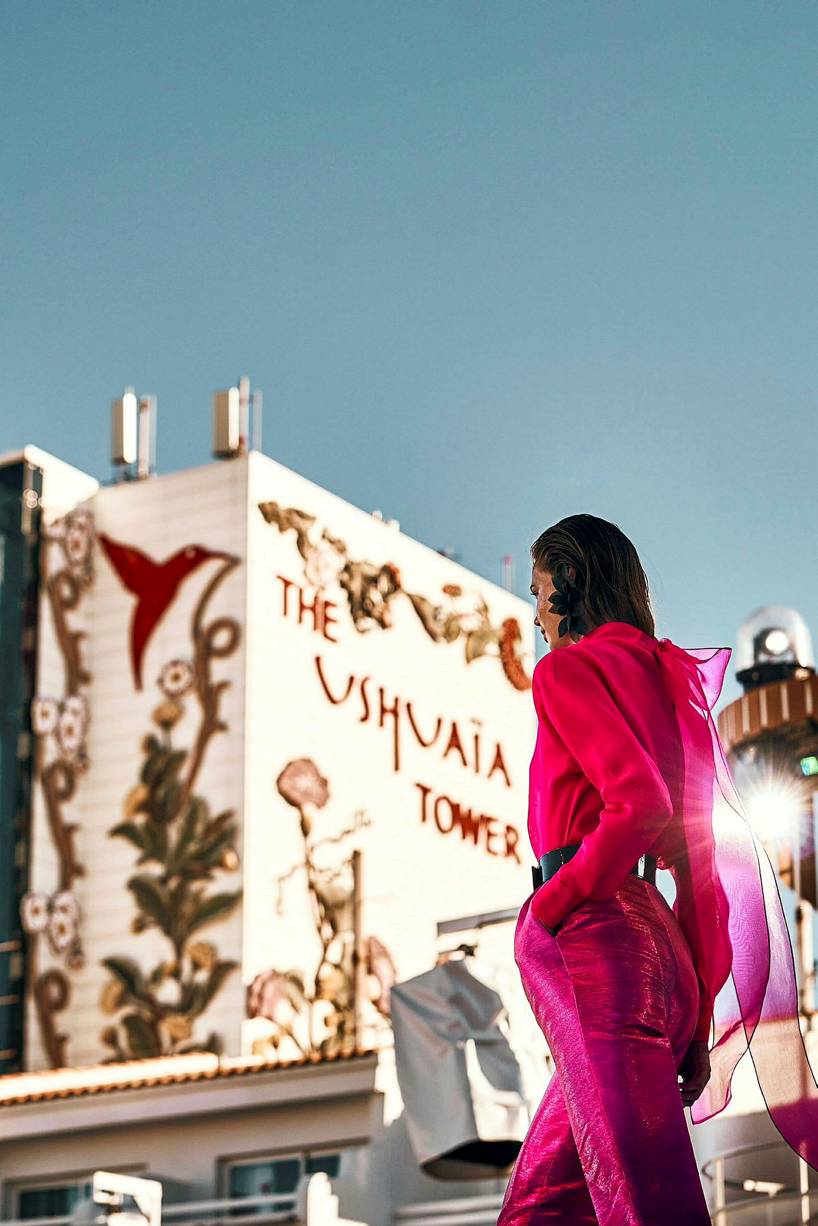 En person i rosa antrekk foran en bygning med teksten 'Ushuaia Tower' og dekorasjoner. (AI-generert tekst)