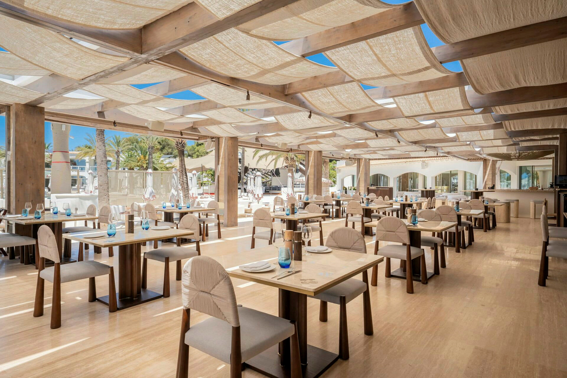 En restaurant med trebord og stoler, godt opplyst med naturlig lys. (AI-generert tekst)
