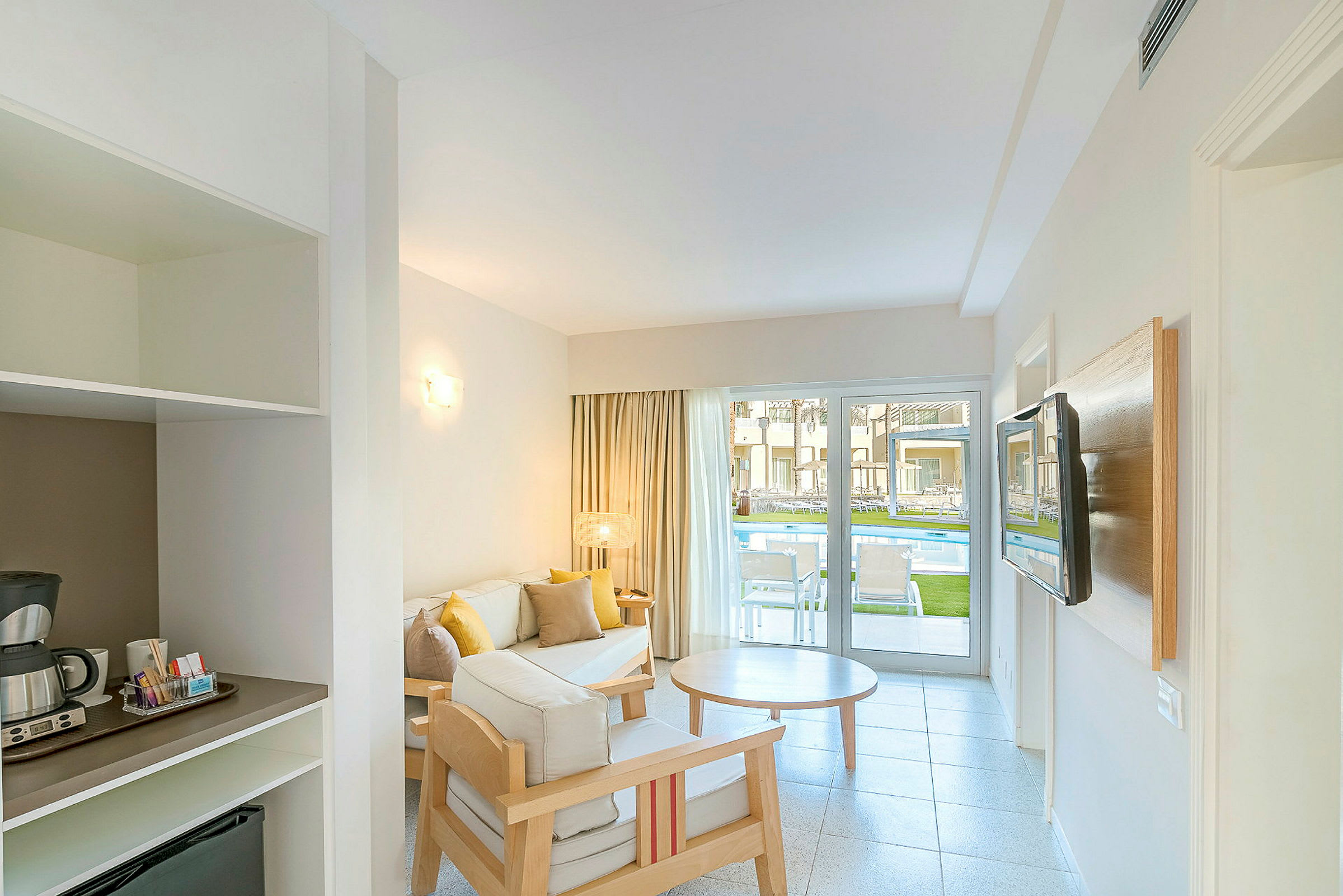 Hotellrom med sittegruppe og utsikt mot bassenget gjennom en glassdør. (AI-generert tekst)