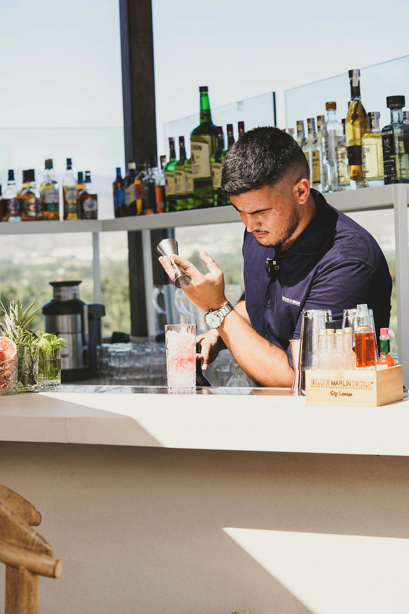 En bartender ved en bar med flasker og drikker på hyller. (AI-generert tekst)