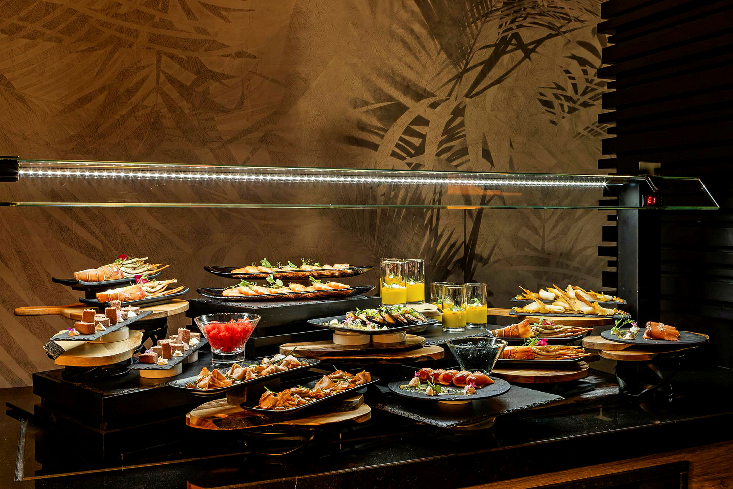 Et buffébord med forskjellige retter og desserter lagt opp på tallerkener og glass, under en glasskuppel. (AI-generert tekst)