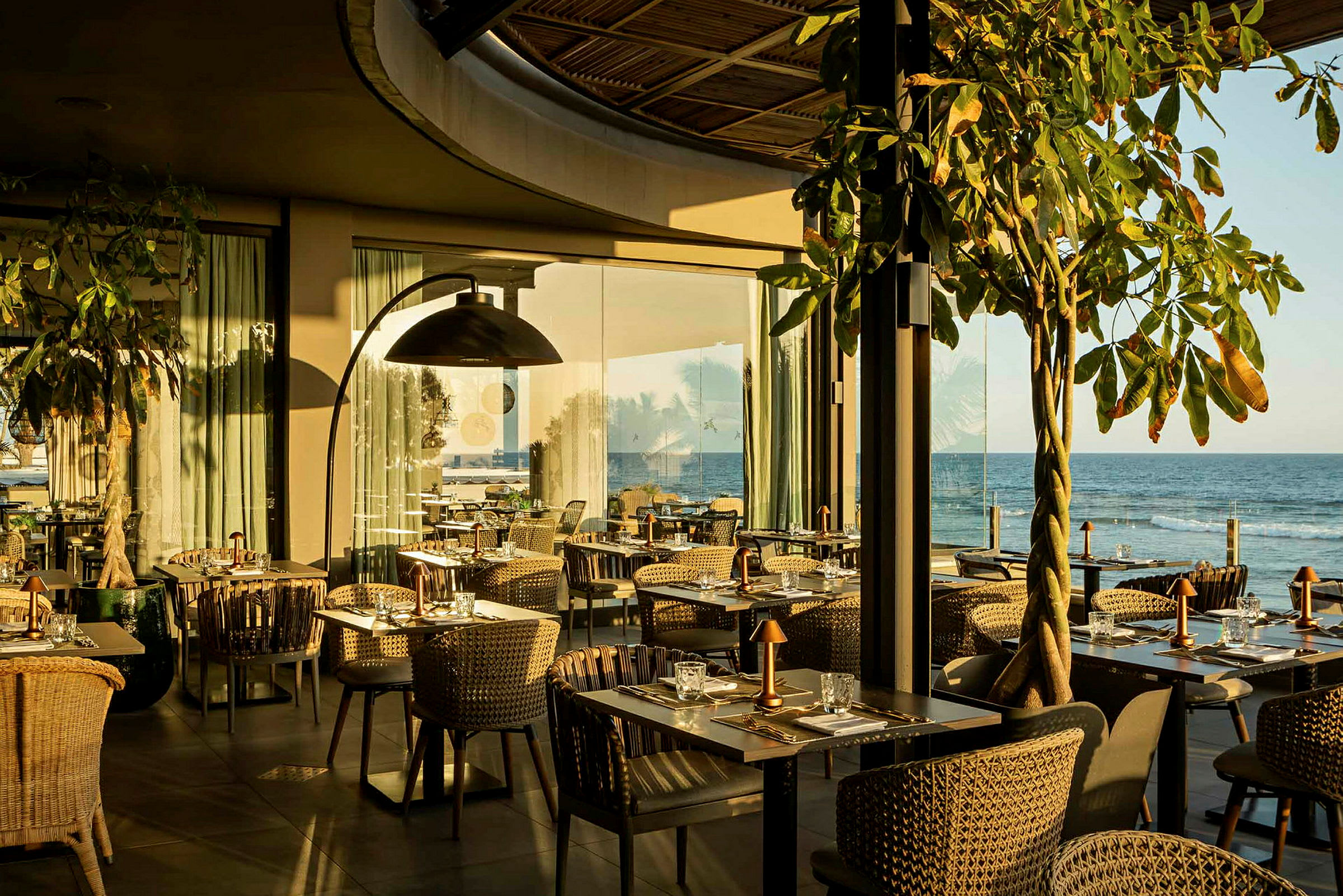 En restaurant med bord og stoler nær havet, i sollys. (AI-generert tekst)