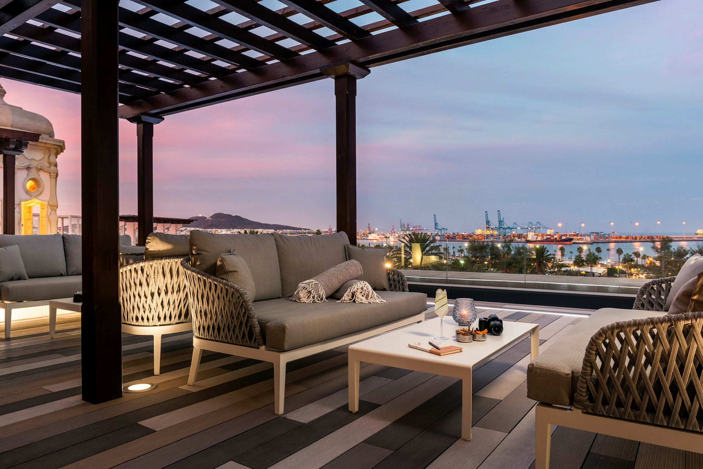 Moderne sittegruppe på terrasse med utsikt over havn og by i skumringen. (AI-generert tekst)