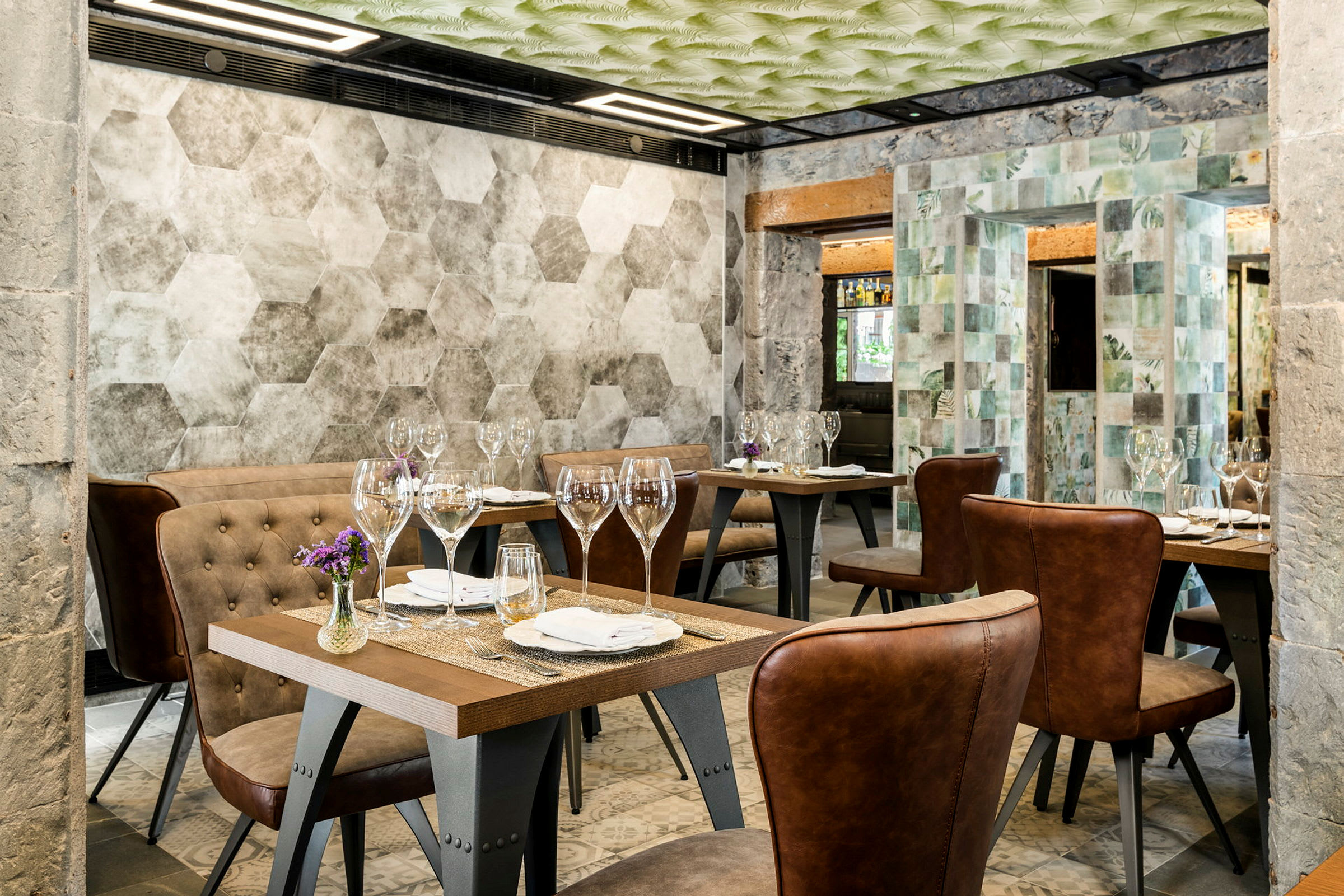 En restaurant med flere bord, oppdekket med glass og servietter. Stolene har brunt skinn, og veggene har geometriske mønstre. (AI-generert tekst)