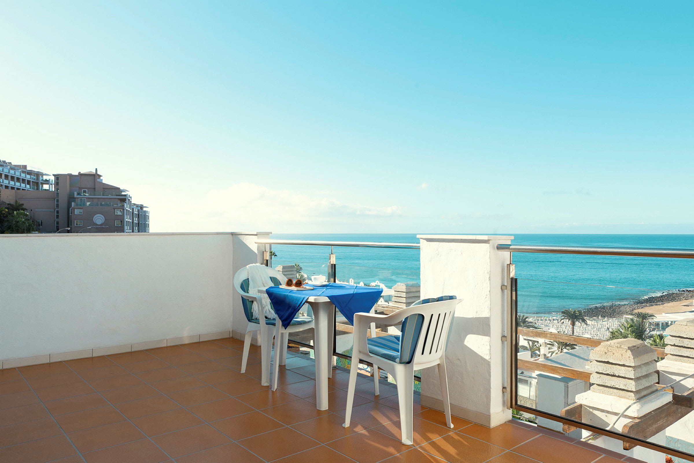 En terrasse med et dekket bord og to stoler, med utsikt over havet og stranden. (AI-generert tekst)