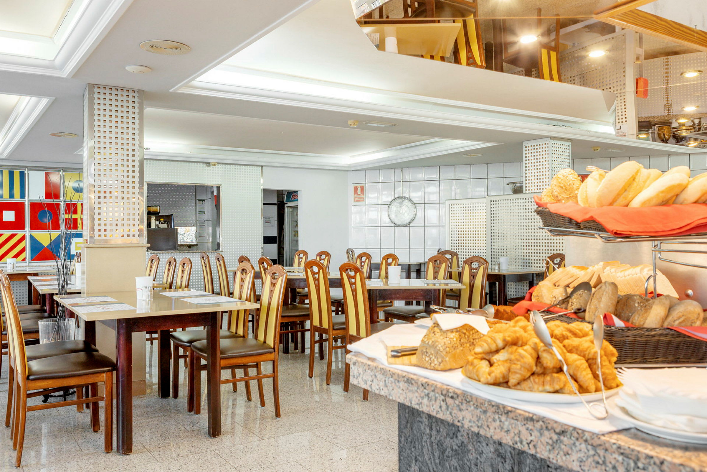 En restaurant med bord og stoler, med brød og bakverk plassert på et bord i forgrunnen. (AI-generert tekst)