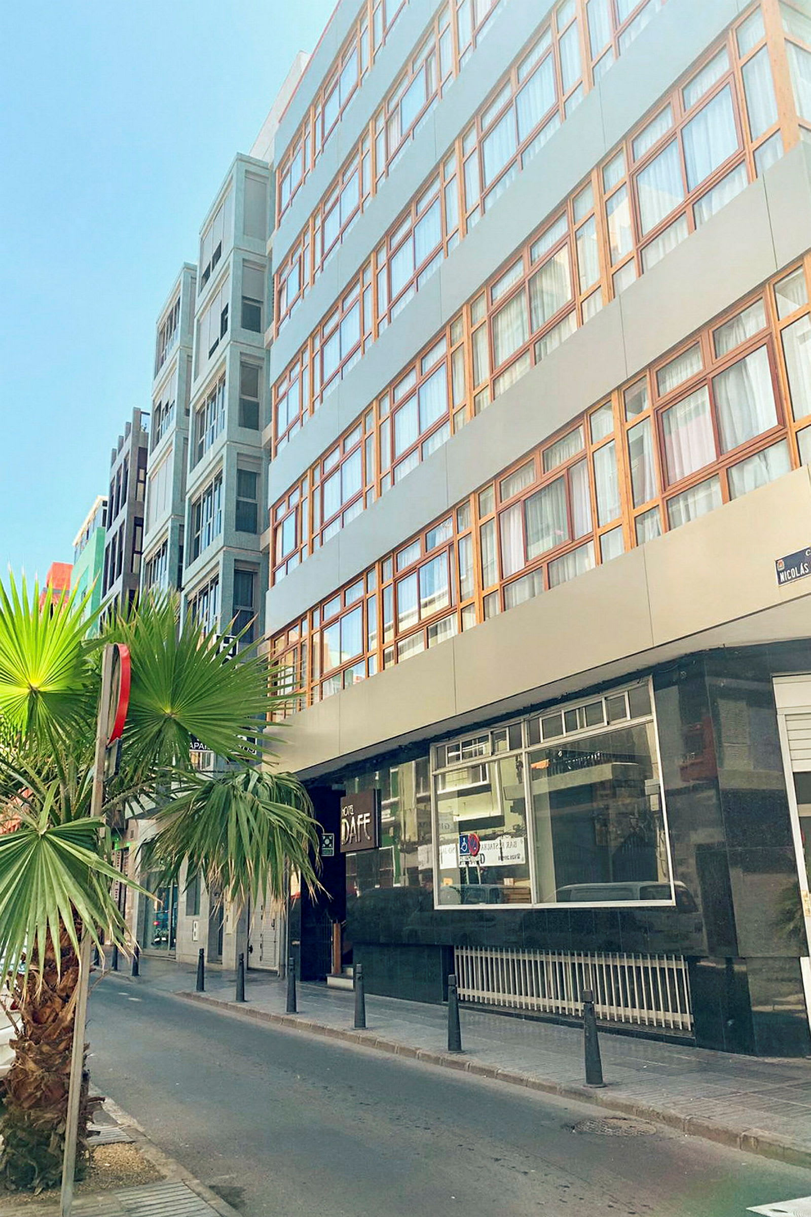 Bygning med flere etasjer og store vinduer, og en gate med palmer utenfor. (AI-generert tekst)