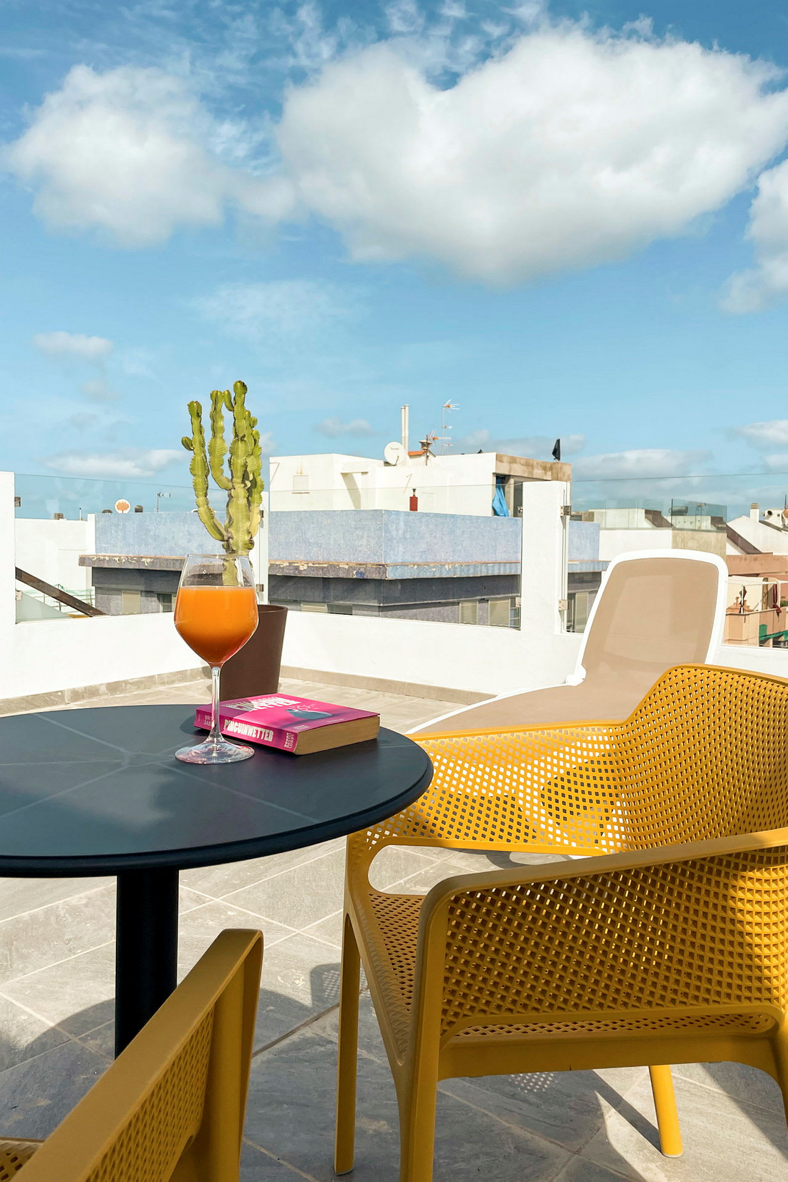 En terrasse med et bord, en bok og et glass juice. (AI-generert tekst)