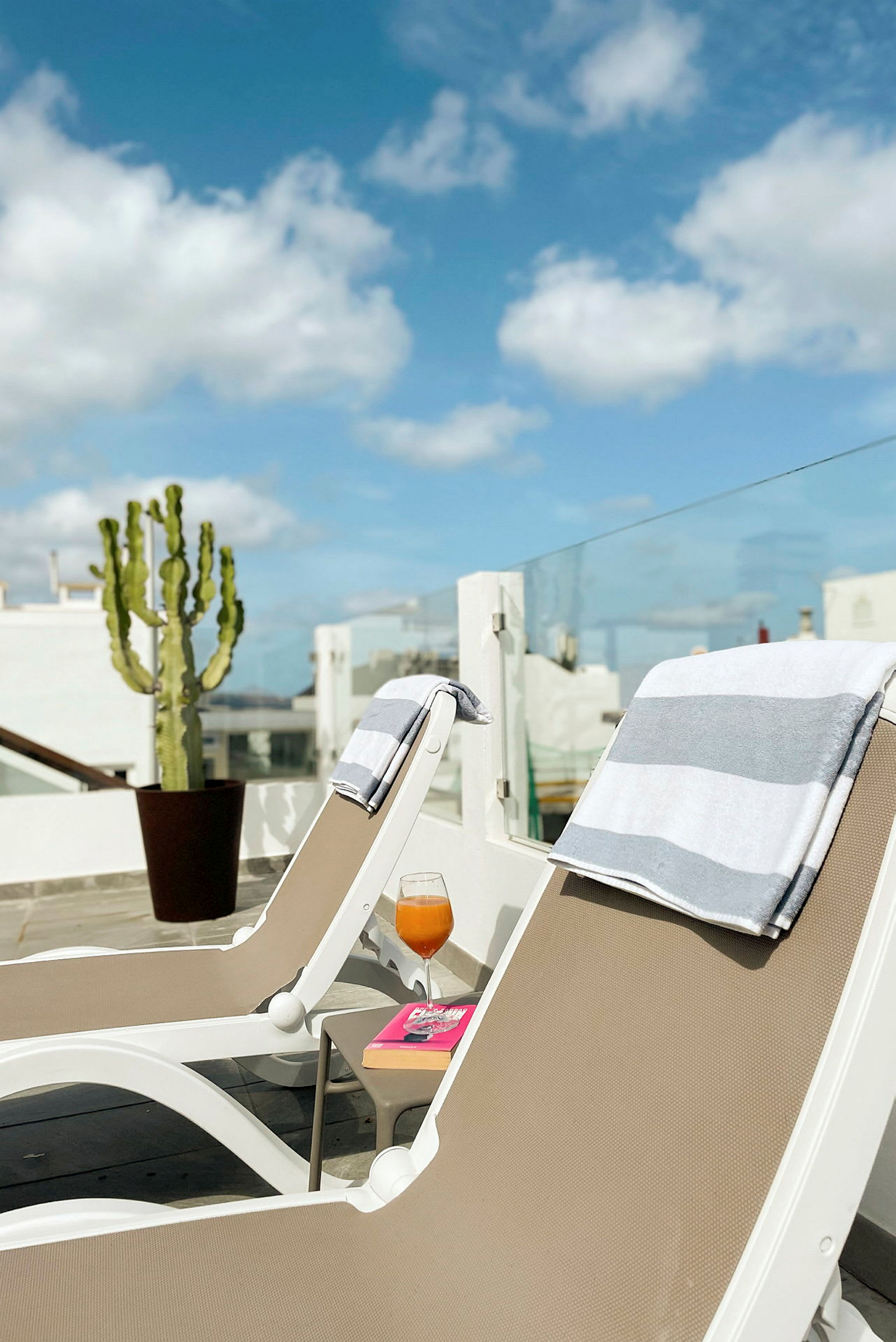 To solsenger med håndklær på en terrasse, en drink og en bok på et bord ved siden av. (AI-generert tekst)
