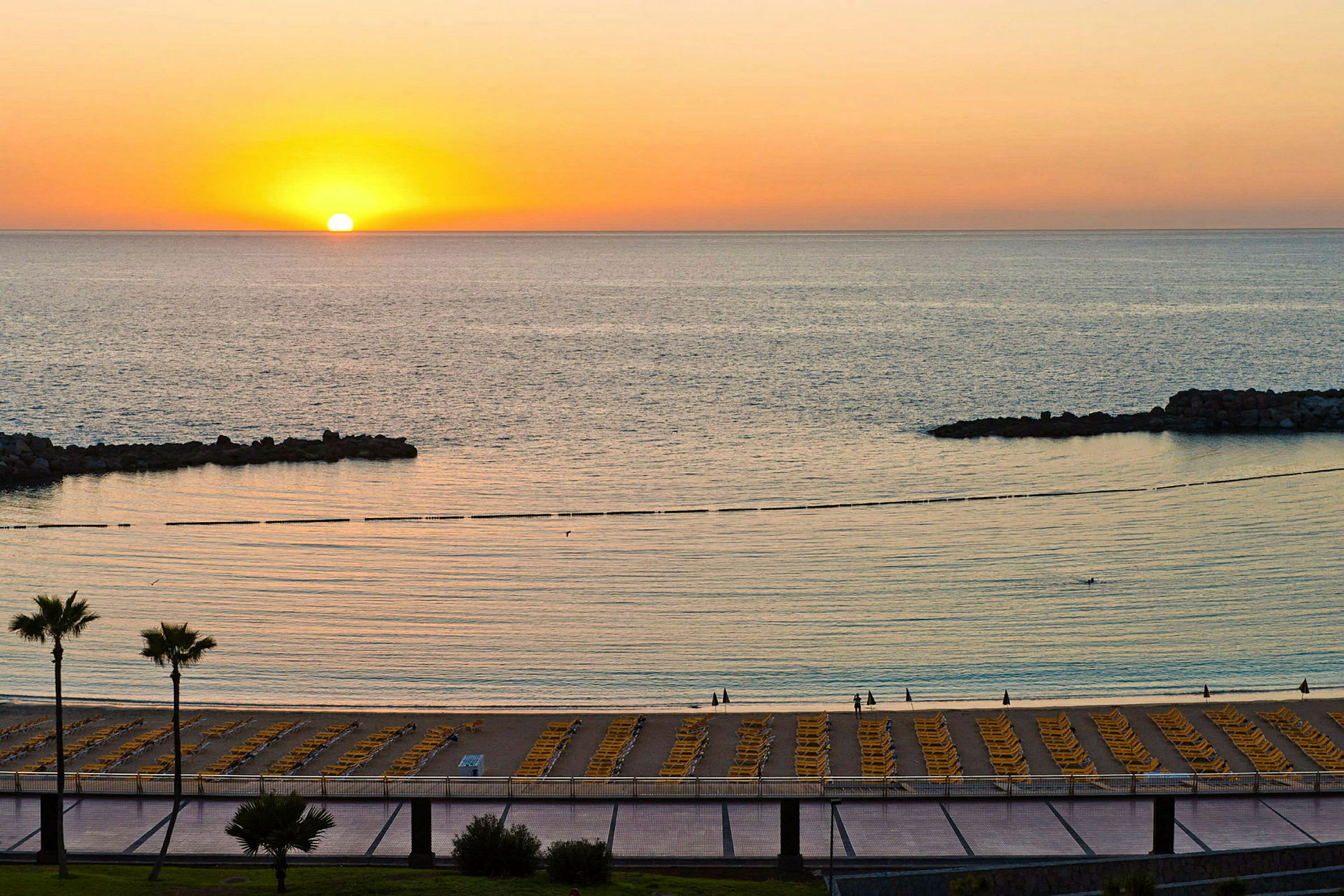 Solnedgang over en strand med solsenger og havet. (AI-generert tekst)