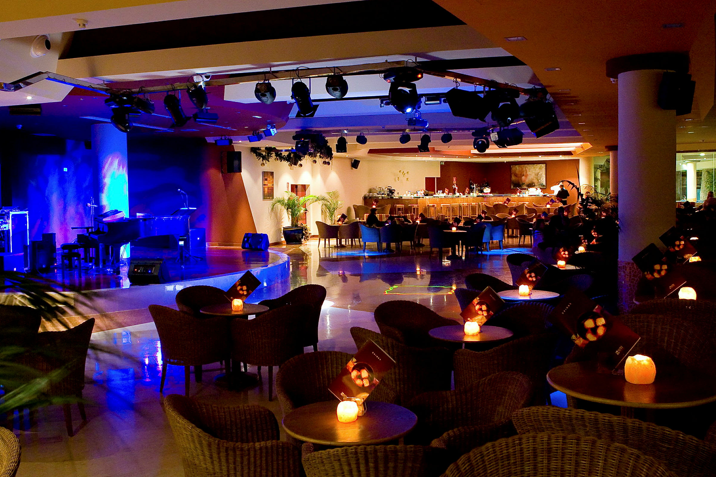 Interiør av en opplyst bar og scene med sitteplasser rundt små bord. (AI-generert tekst)