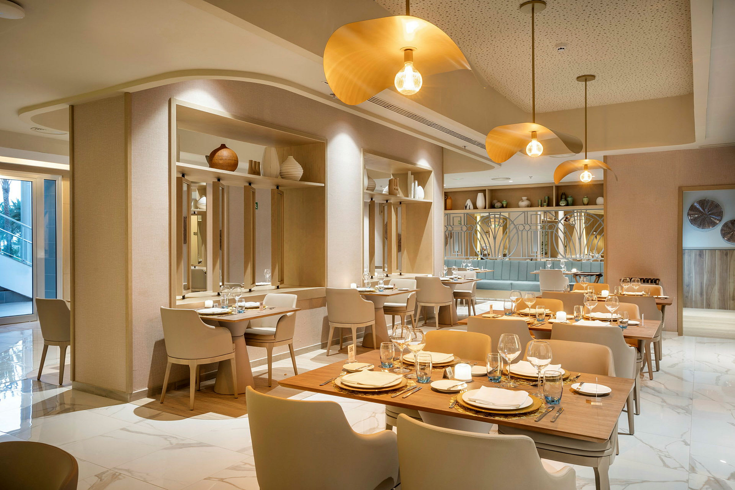 En elegant og moderne restaurant med trebord, lyse stoler og gyldne belysningsarmaturer. (AI-generert tekst)