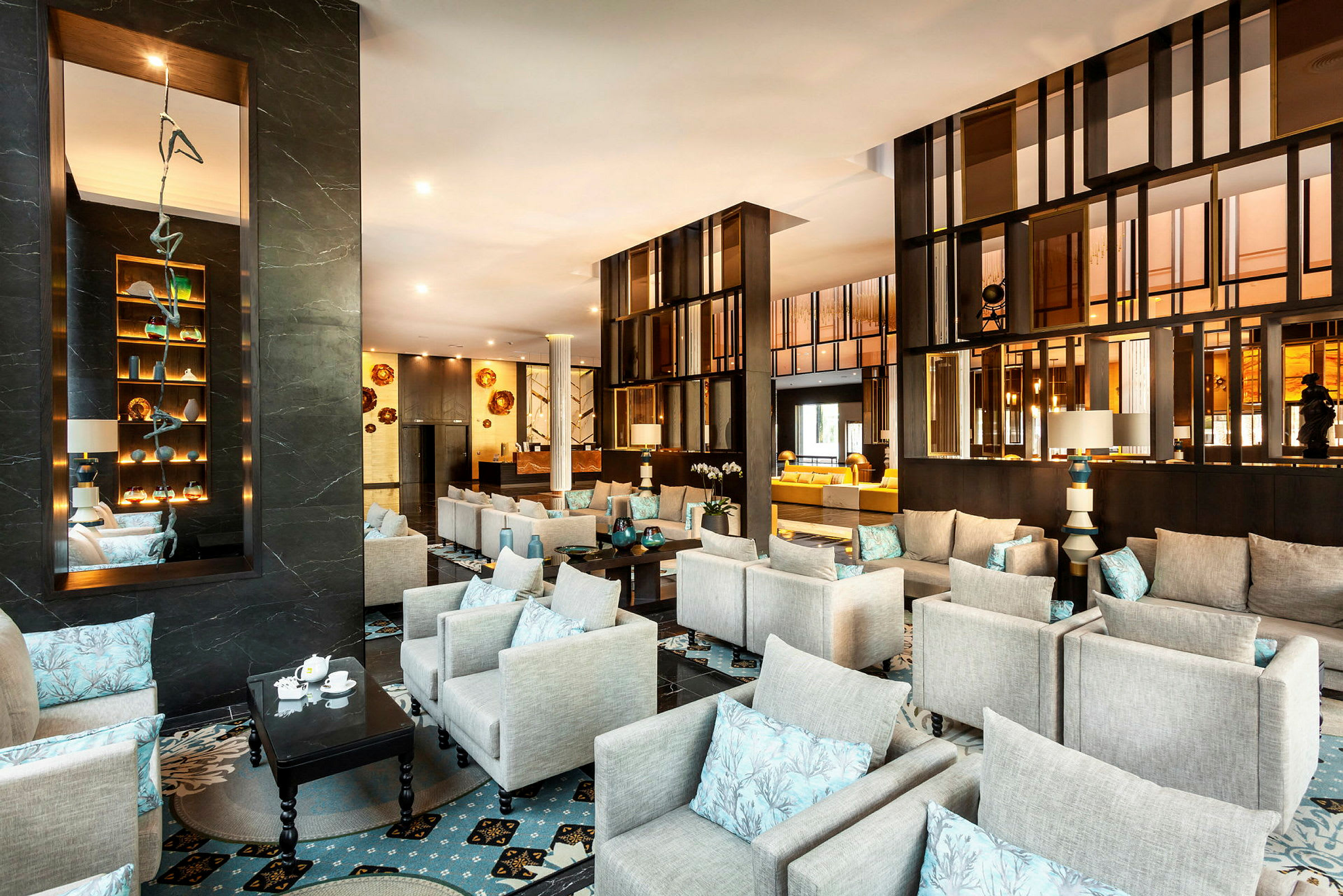 Et moderne og stilfullt innredet loungeområde med grå lenestoler, blå puter og elegant borddekorasjon. (AI-generert tekst)