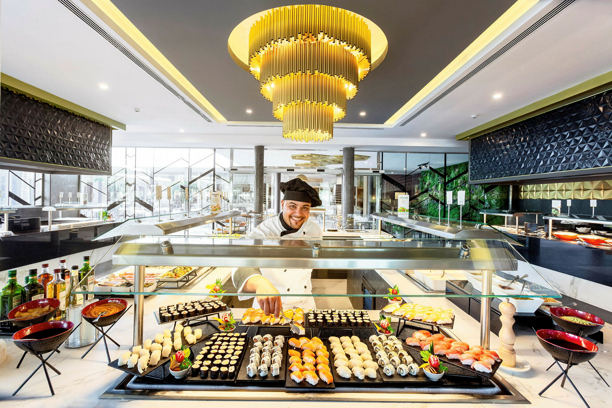 En elegant matservering med sushi og andre småretter på en buffé, opplyst av en luksuriøs lysekrone. (AI-generert tekst)